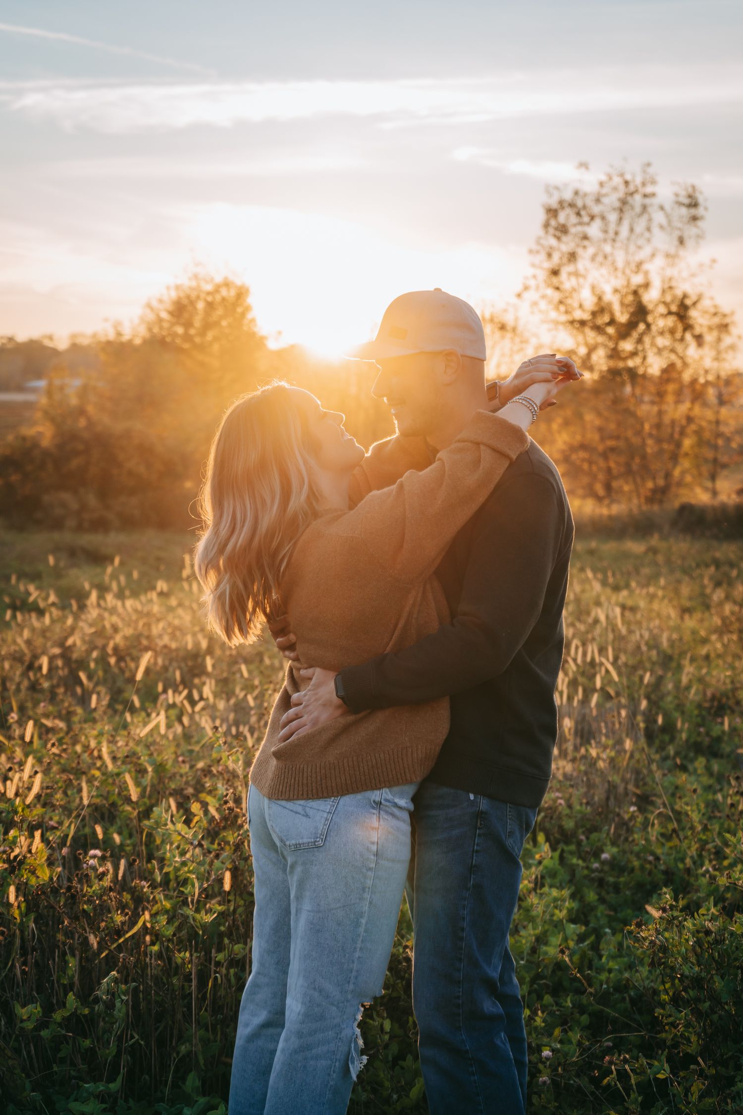 Romantic engagement photo of couple embracing at sunset in a dreamy field in the Finger Lakes with warm light and tall grass