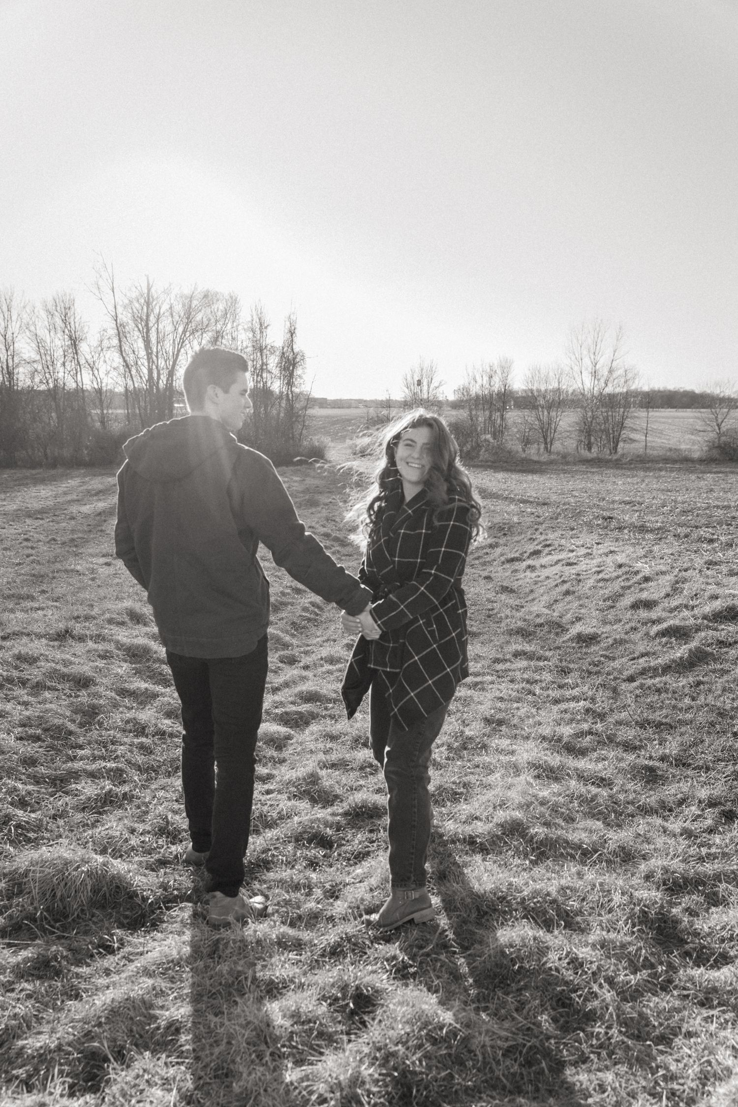 Black and white engagement photo of a couple holding hands in a Finger Lakes field, capturing movement and connection
