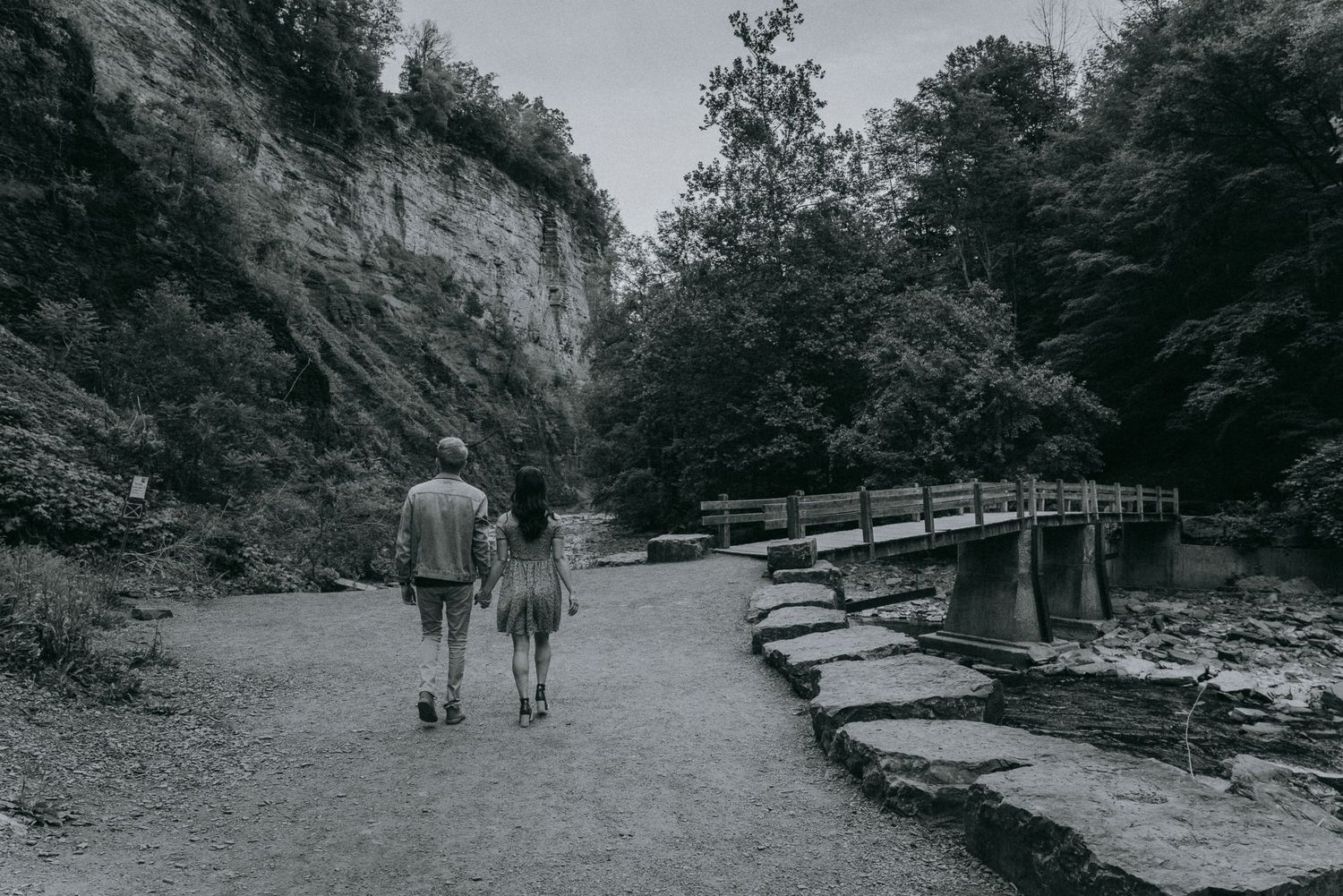 Black and white engagement photo of couple walking hand in hand near Taughannock Falls State Park in the Finger Lakes, NY