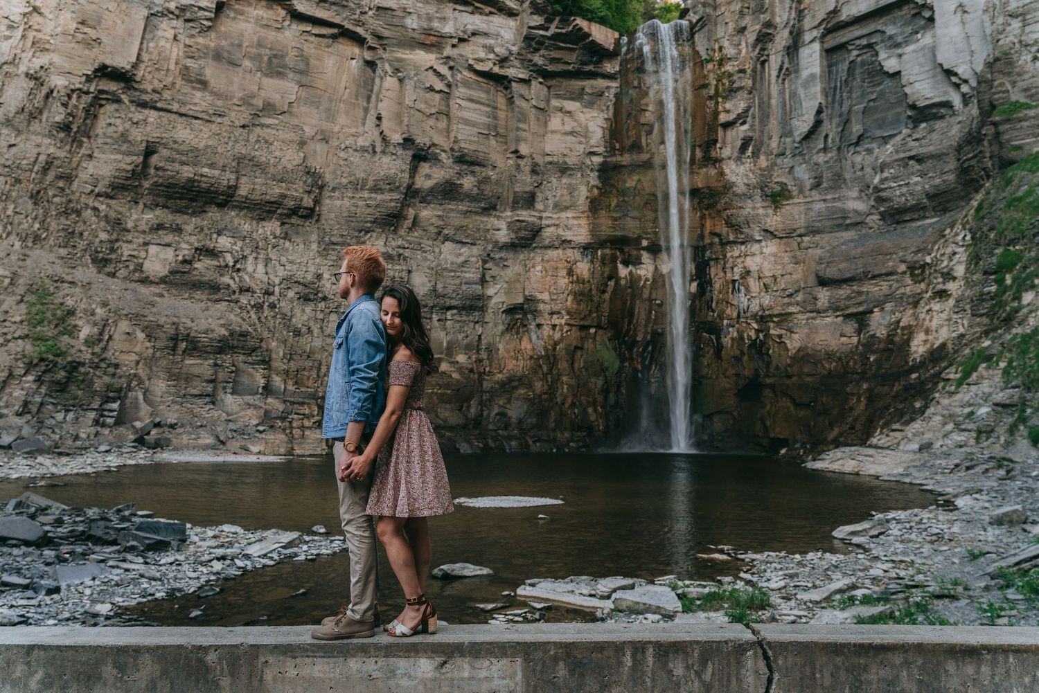 Wide engagement photo of couple embracing near Taughannock Falls surrounded by stone cliffs in Ithaca, New York