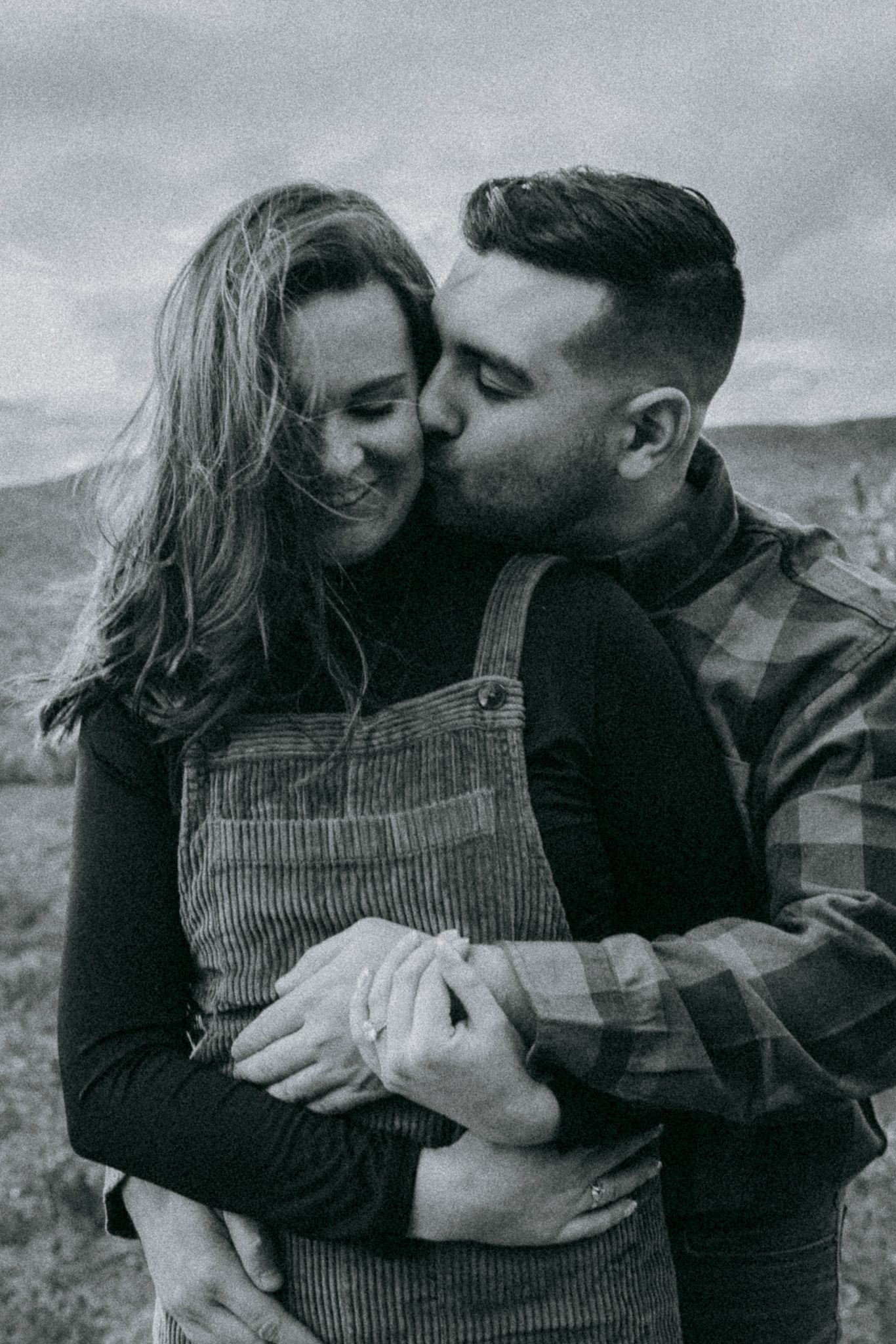 Black-and-white engagement photo of a couple holding each other on Rattlesnake Mountain, overlooking Squam Lake in New Hampshire