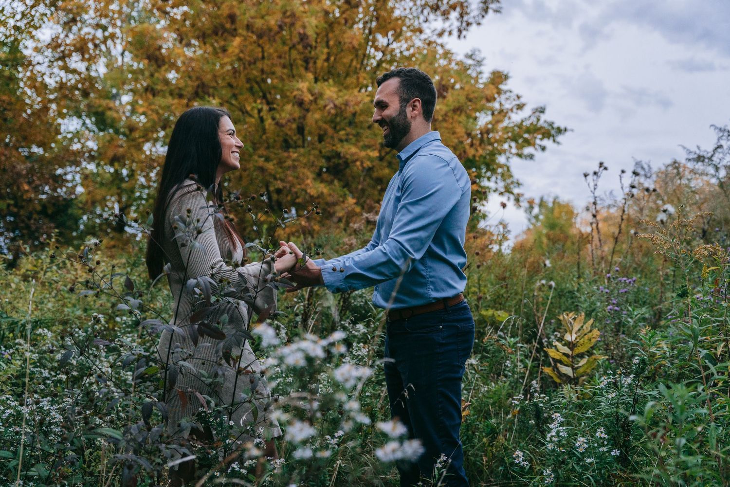 Engaged couple holding hands in flowery autumn field during Geneva NY engagement session near Seneca Lake in the Finger Lakes region