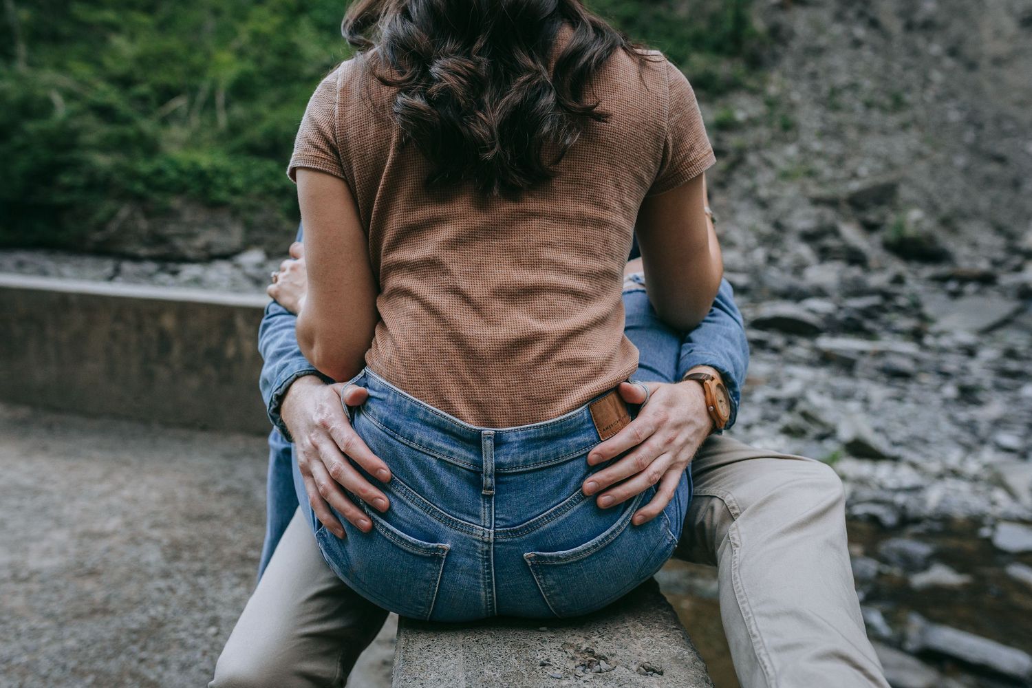 Romantic engagement photo of couple sitting together near Taughannock Falls with dramatic rock cliffs in the Finger Lakes region of New York