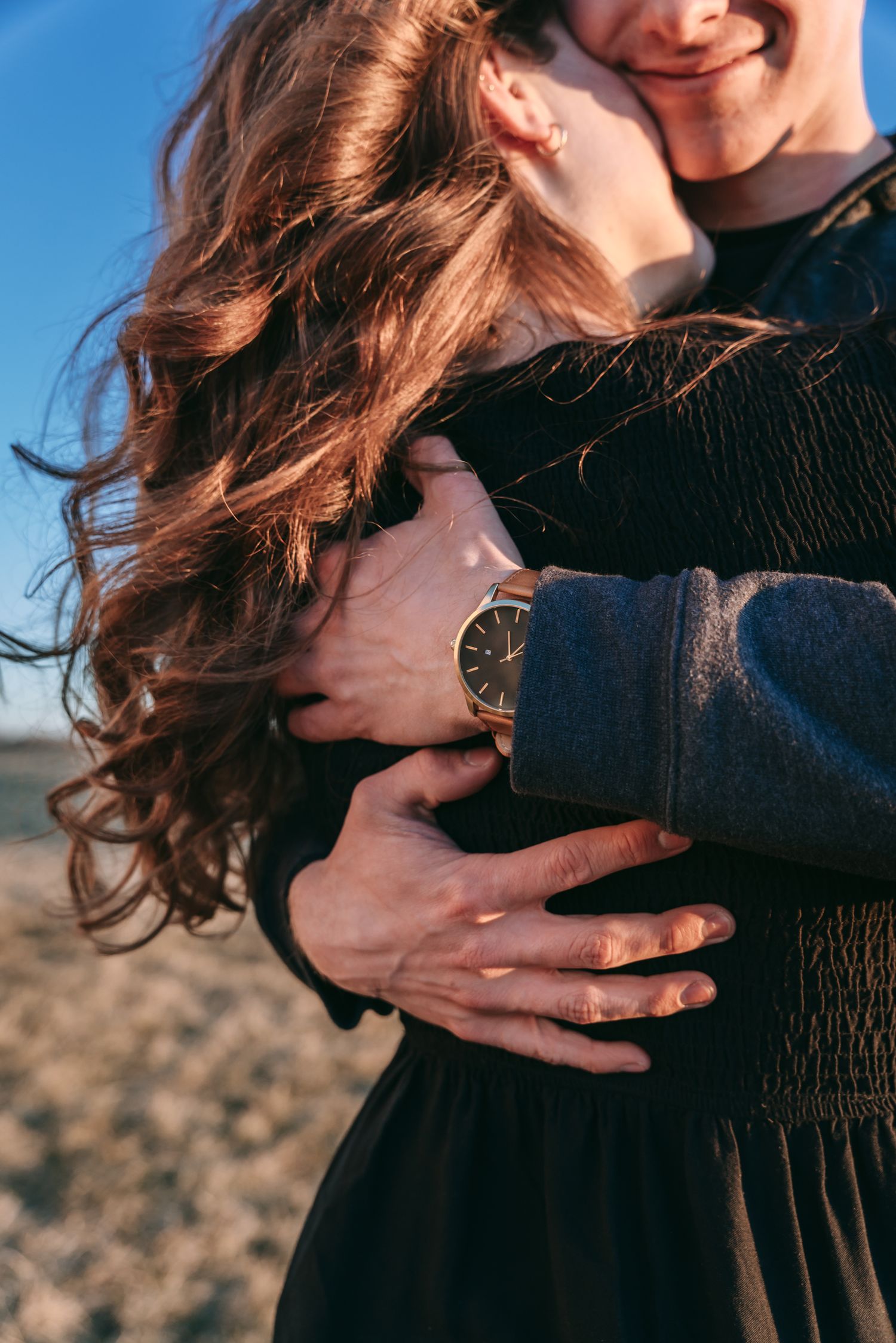 Close-up engagement photo showing a couple’s embrace, flowing hair, and engagement ring in a Finger Lakes field