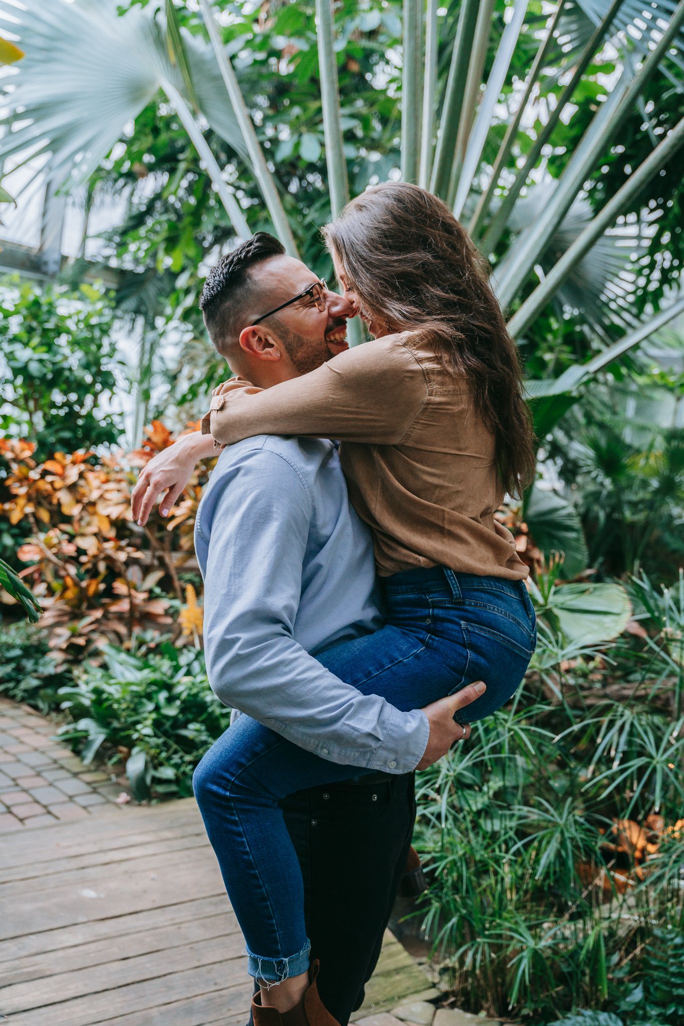 Engaged couple giggling and laughing among lush greenery at Highland Park Conservatory in Rochester NY, intimate engagement session indoors