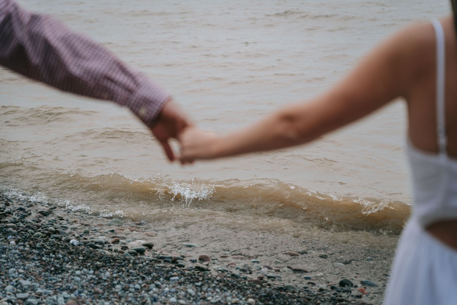 Couple holding hands by the water’s edge during Rochester NY engagement session, candid Finger Lakes wedding photography style