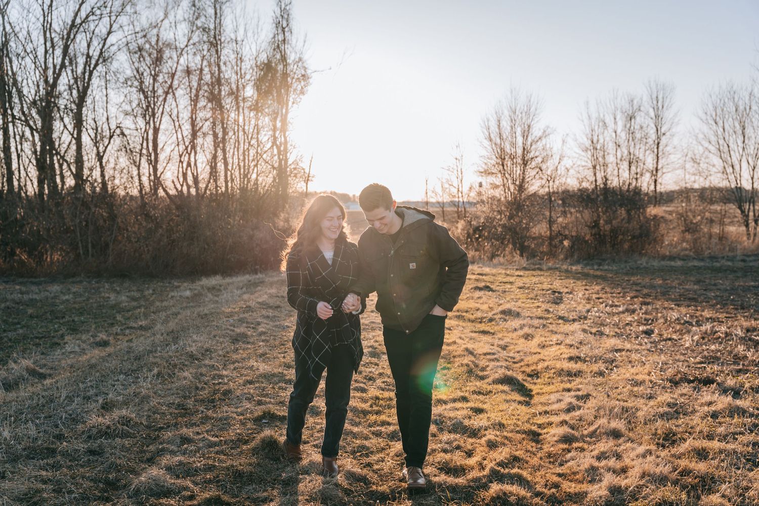 Engagement session in the Finger Lakes with a couple walking hand in hand through an open field at golden hour