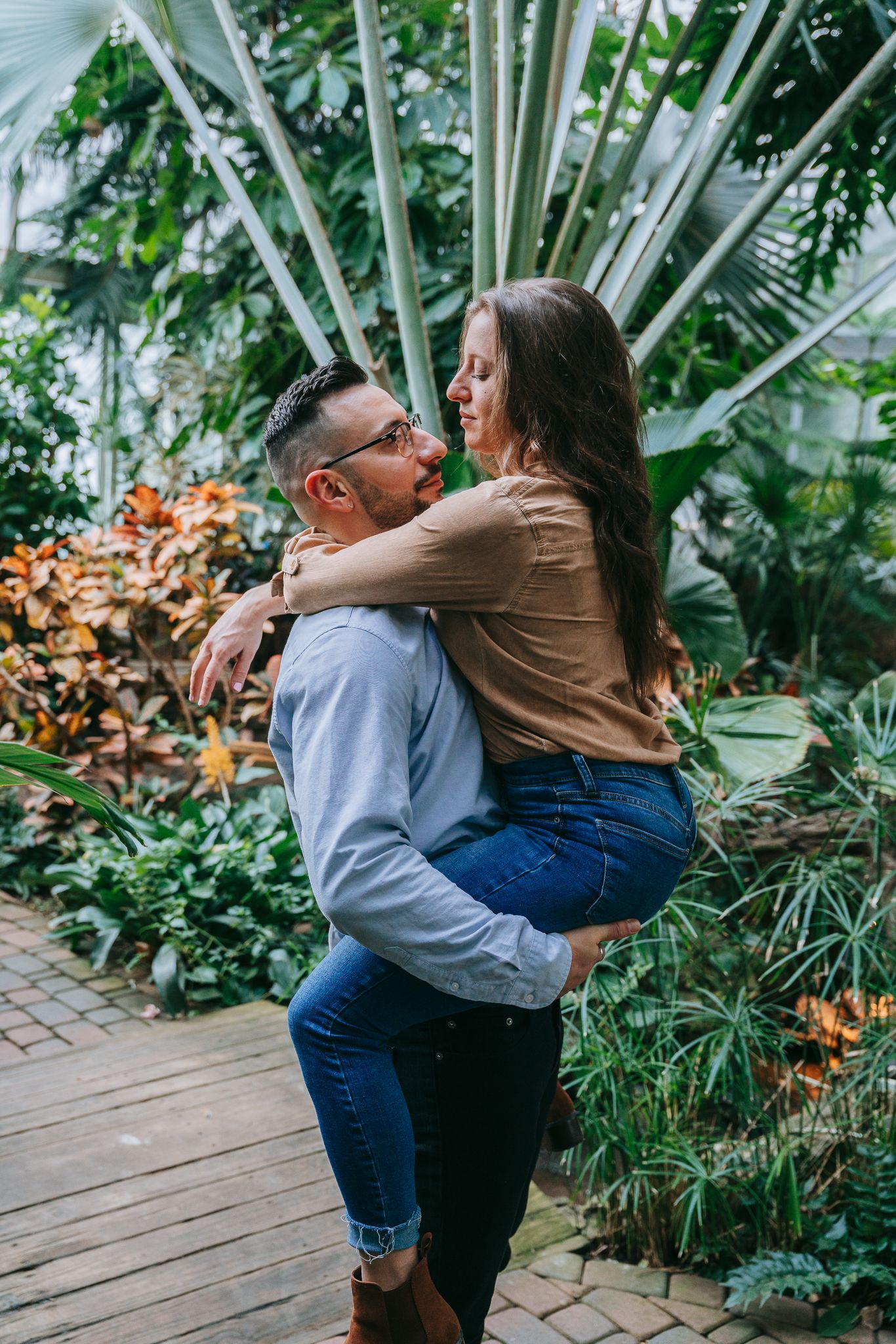 Engaged couple embracing among lush greenery at Highland Park Conservatory in Rochester NY, intimate engagement session indoors