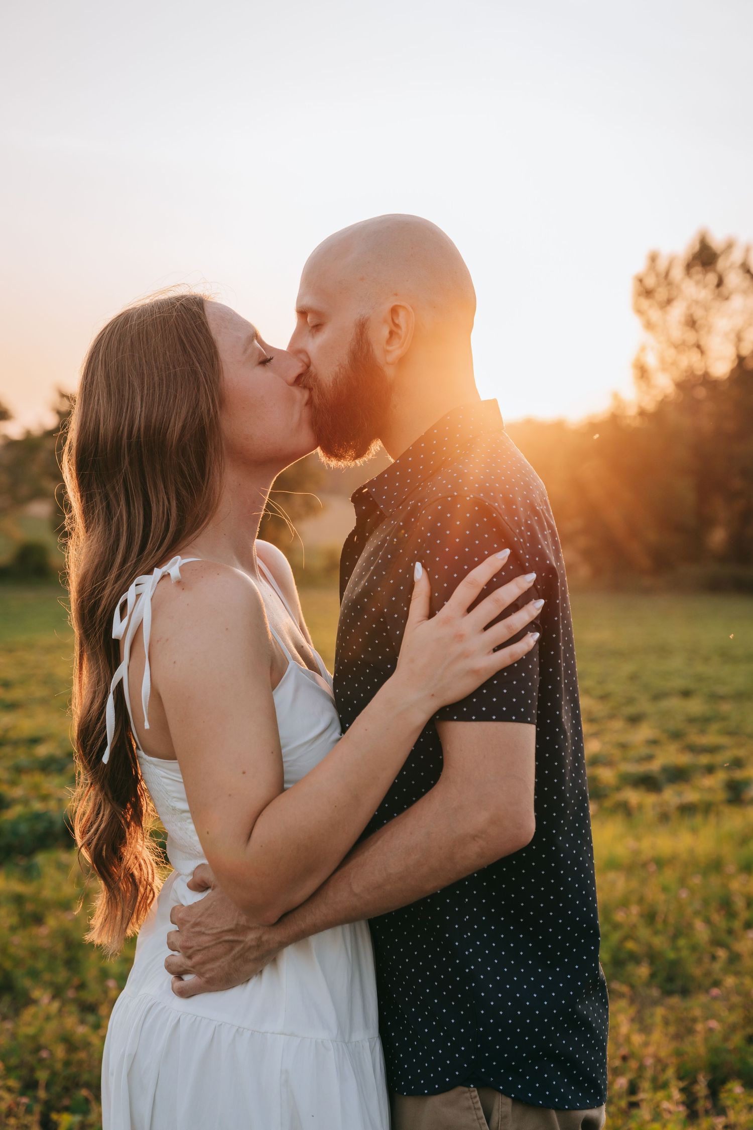 Engaged couple kissing at golden sunset in Fingger Lakes NY field mini session, captured by engagement photographer in Upstate NY