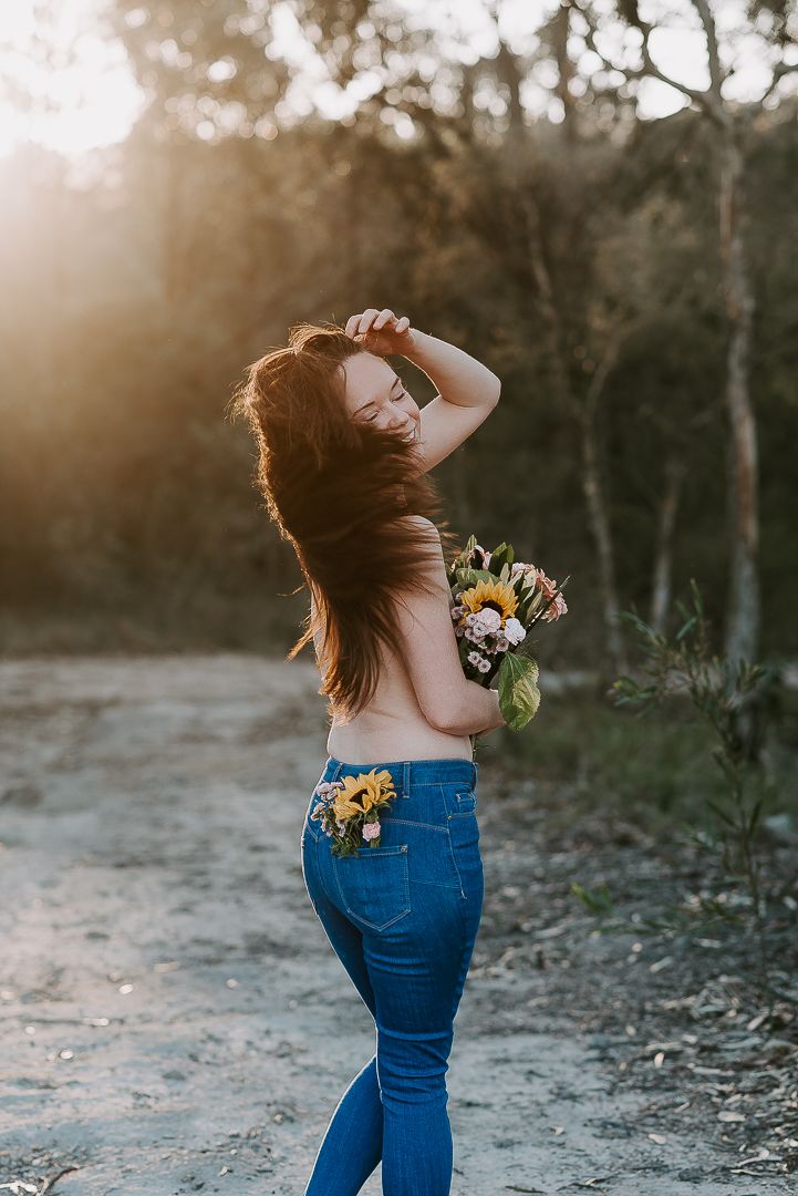 Woman poses with flowers as golden sun sets behind her for boudoir photographer SeduXion Studio in Perth Western Australia