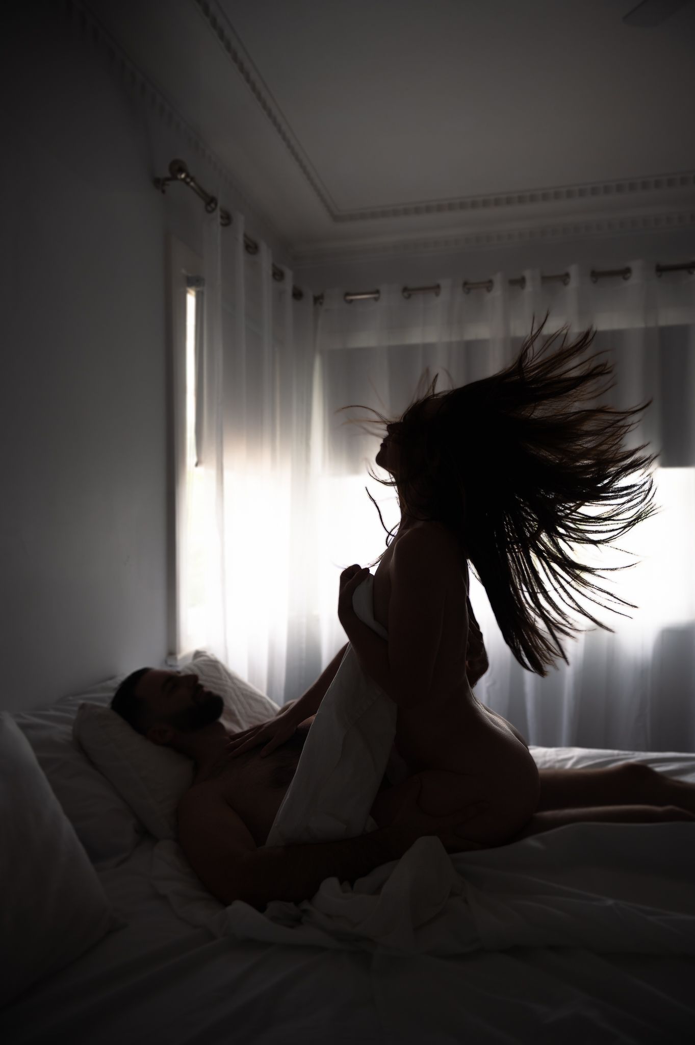 Silhouetted photograph of couple on bed posing affectionately in dark clothing for couples boudoir photoshoot in Mandurah Western Australia