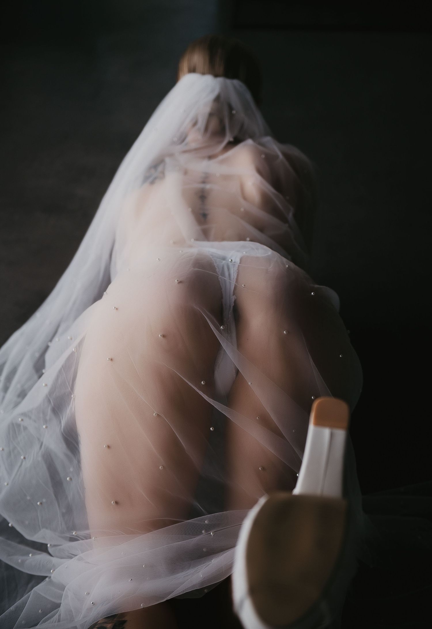 A figure draped in a sheer white veil with pearl details, poses artistically in soft light. Boudoir photoshoot at SeduXion Studio Mandurah