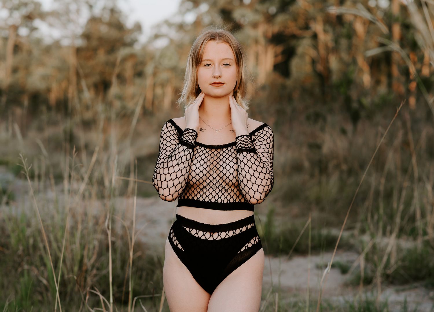 Woman wearing black mesh swimsuit poses outdoors in natural setting during golden hour for boudoir photoshoot Mandurah boudoir photographer