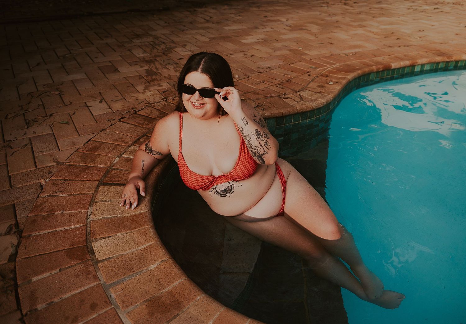 Plus size woman poses in pool in red swimsuit for boudoir photographer SeduXion Studio in Perth WA