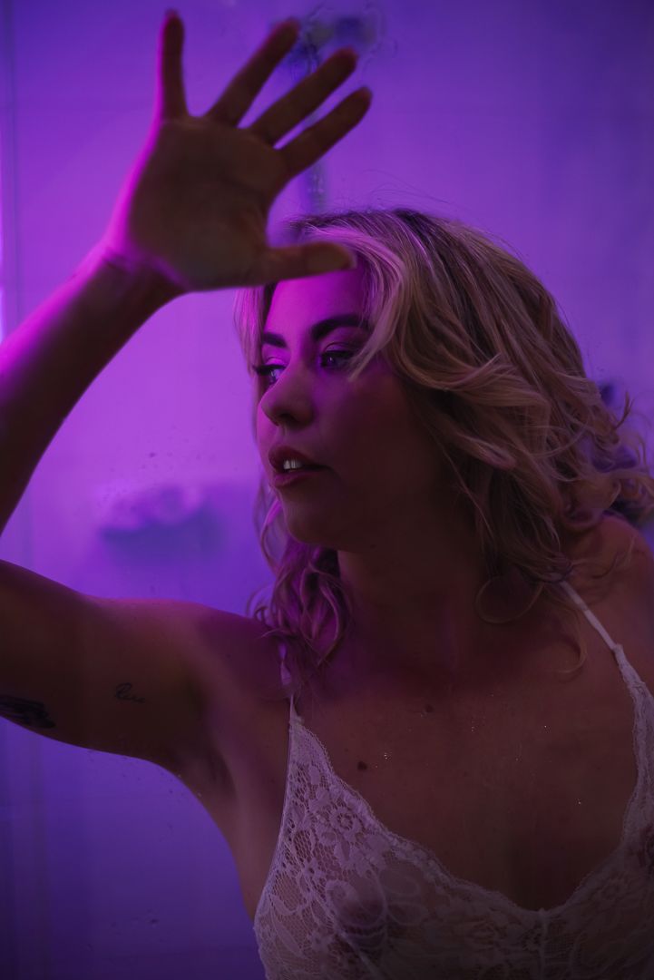 Woman poses in shower with purple neon light in white lingerie for boudoir photographer Mandurah SeduXion Studio