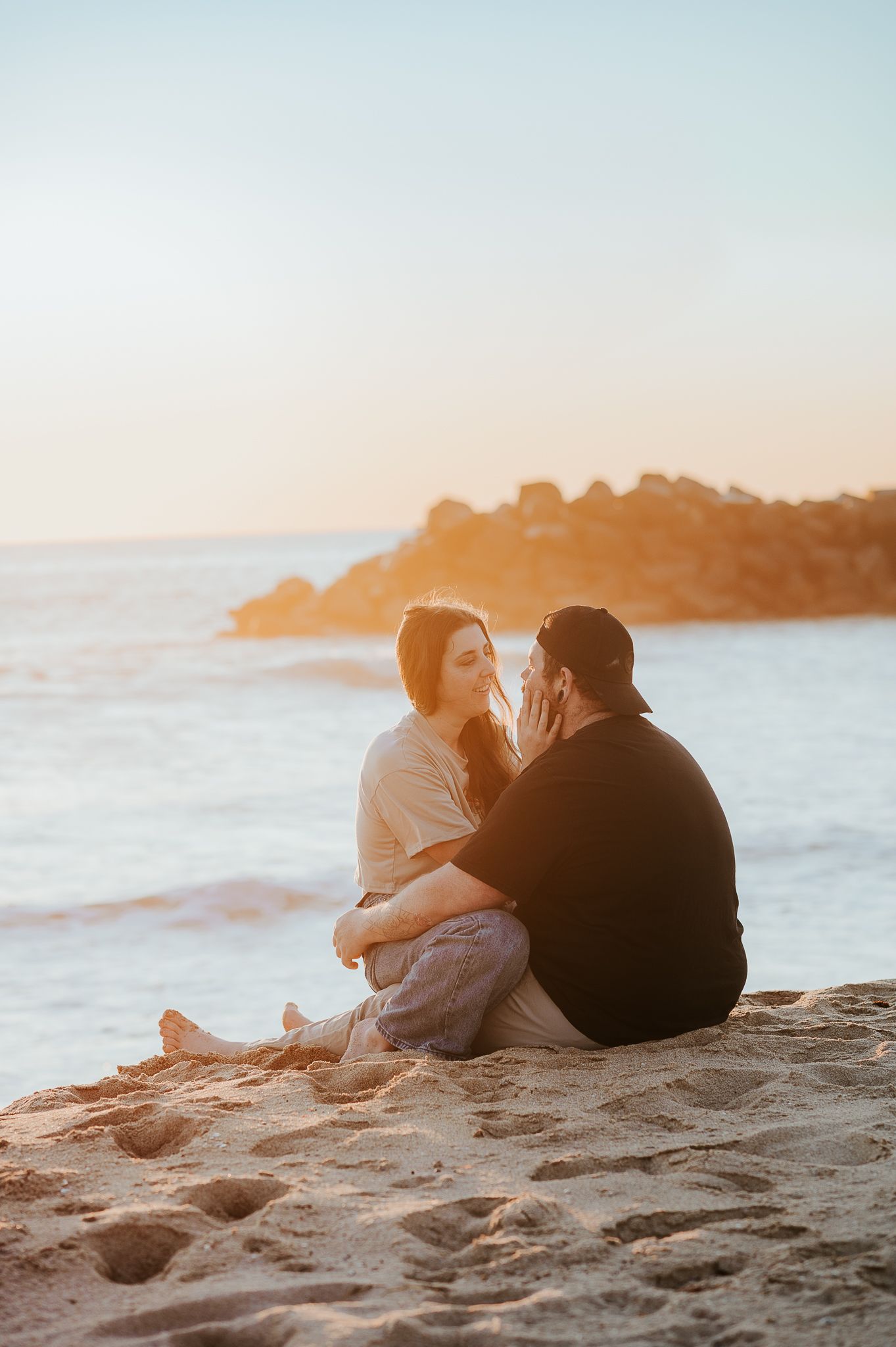 A couple sits together on a sandy beach at sunset watching the waves and ocean view. SeduXion Studio in Mandurah Western Australia