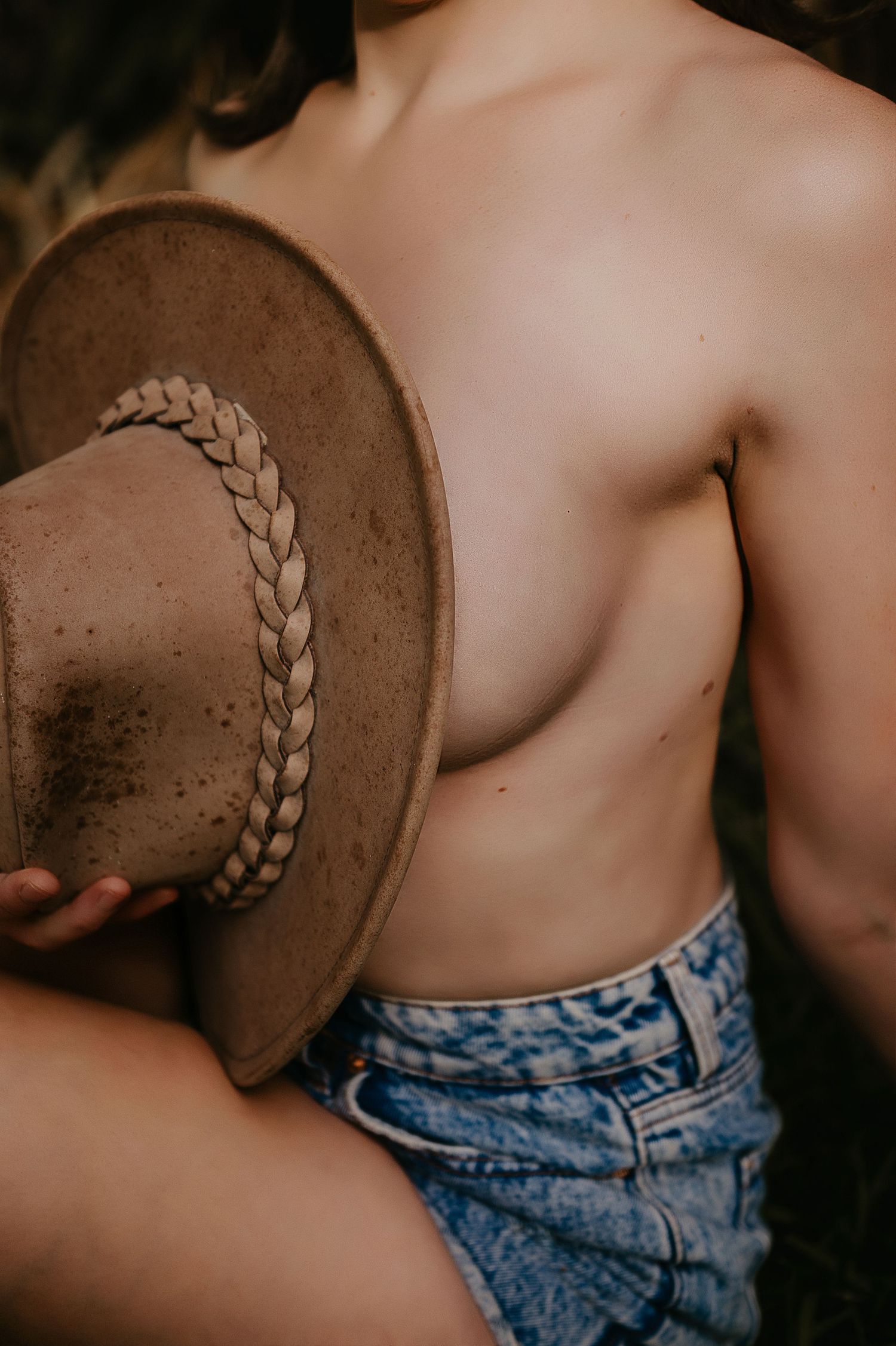 Woman holding a worn brown cowboy hat with braided band, wearing denim shorts in an outdoor setting. Boudoir photographer Perth WA.