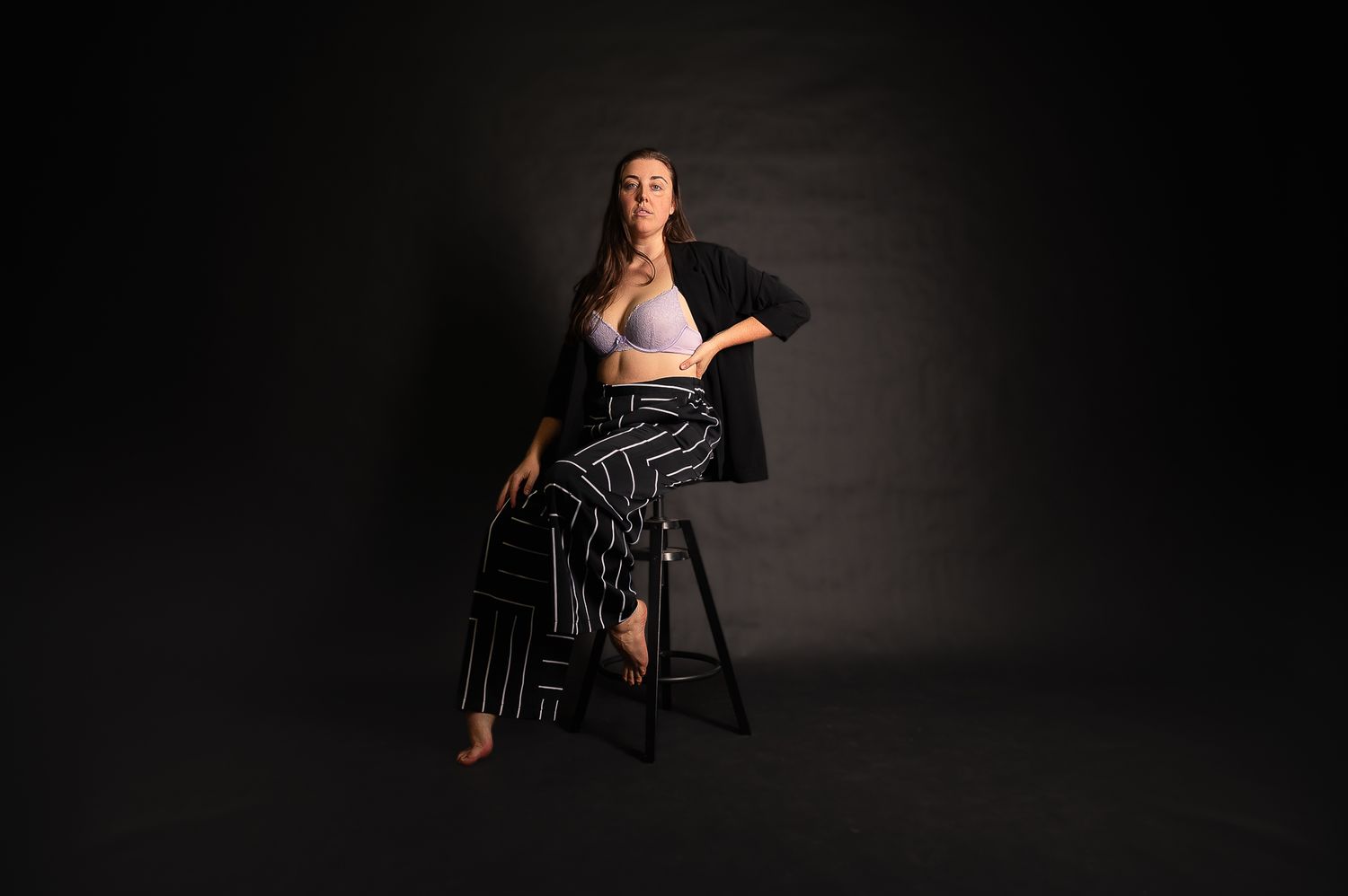Boudoir Photographer, Paige, poses gracefully on a chair against a dark background in a studio setting for SeduXion Studio. Mandurah