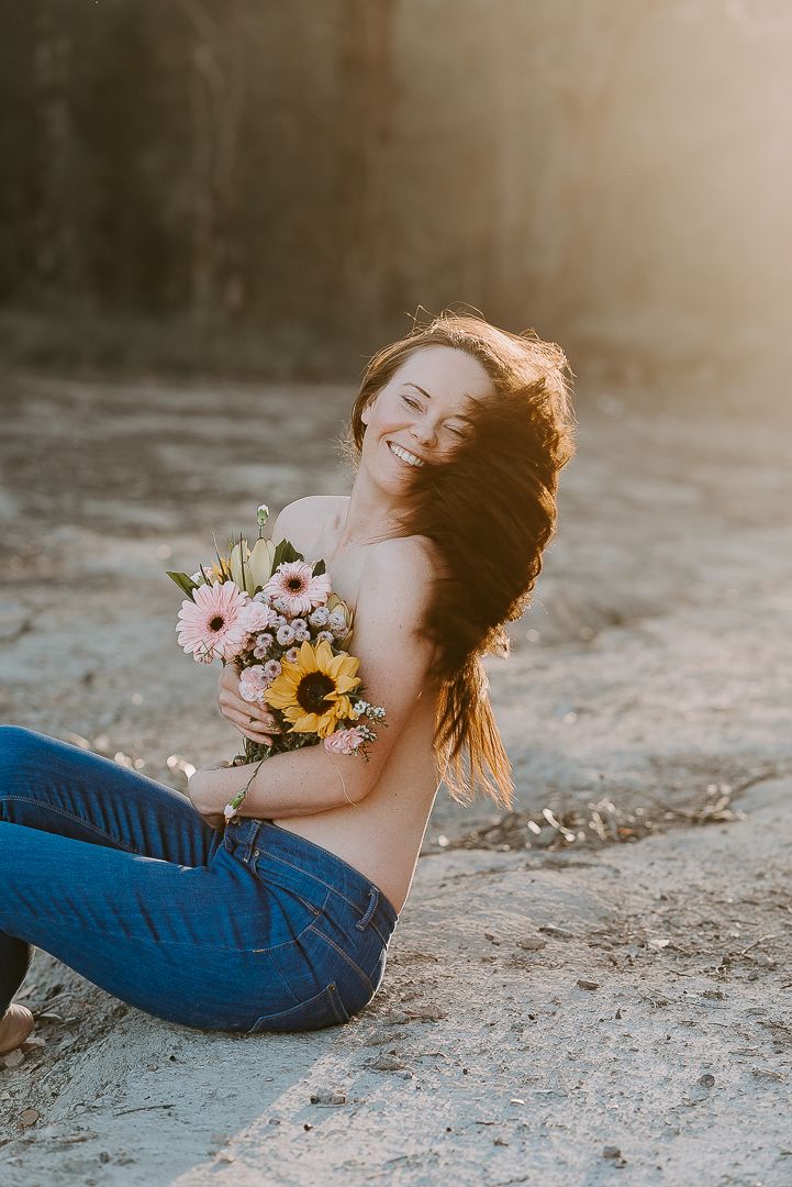 Woman holds flowers to chest under glowing sunset in bushland for boudoir photoshoot with SeduXion Studio in Mandurah Western Australia