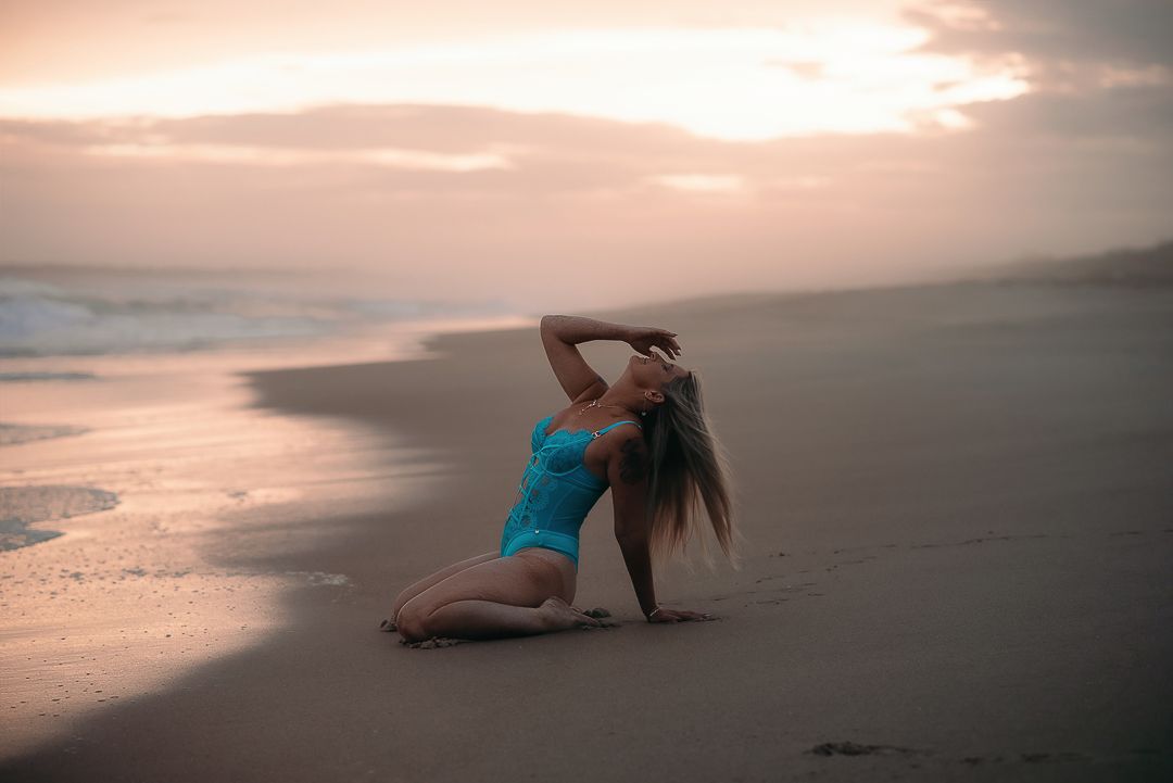 Woman poses on beach, with golden hour sky in the background for outdoor boudoir photoshoot with SeduXion Studio in Mandurah WA