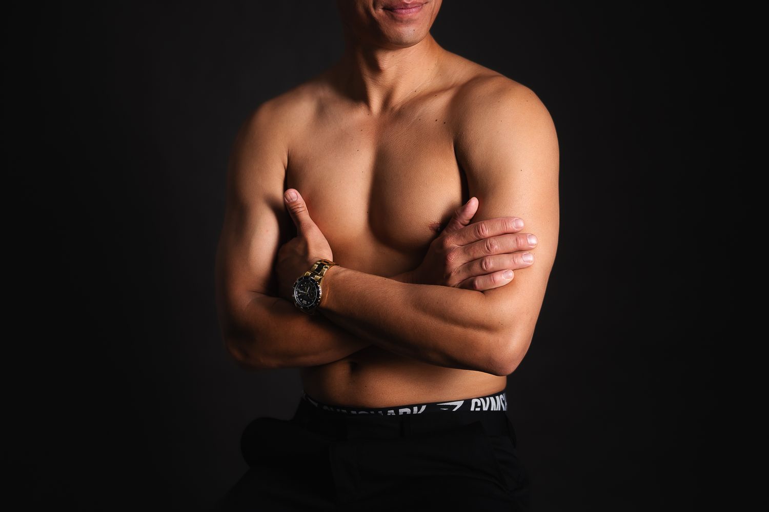 Athletic man with crossed arms stands against dark background showing muscular physique for boudoir photoshoot SeduXion Studio Mandurah
