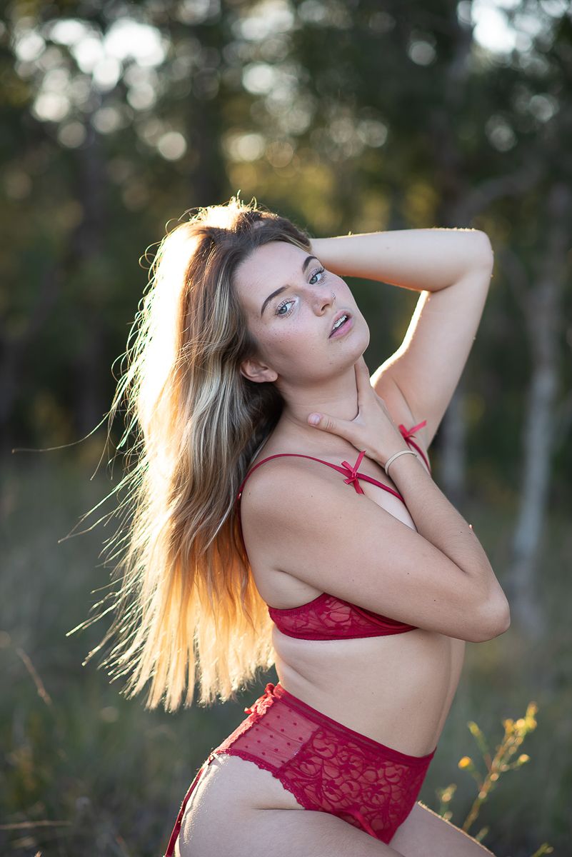 Woman in red lace lingerie poses outdoors with flowing hair in golden sunlight. Mandurah Boudoir Photographer SeduXion Studio