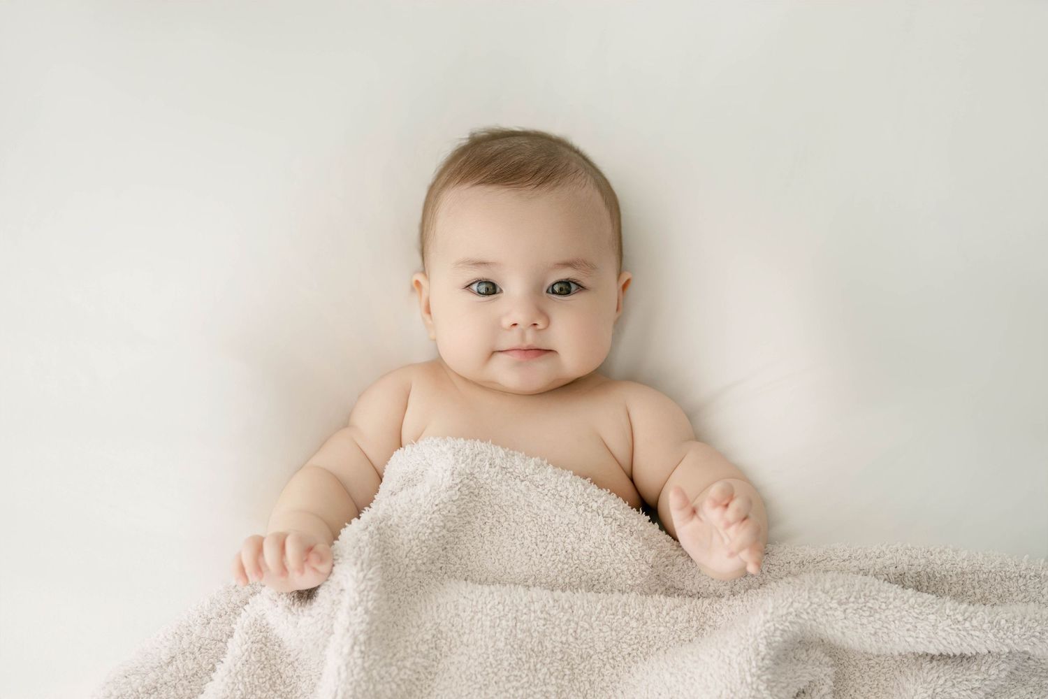 Infant lying on white bedding with soft natural lighting from the side.