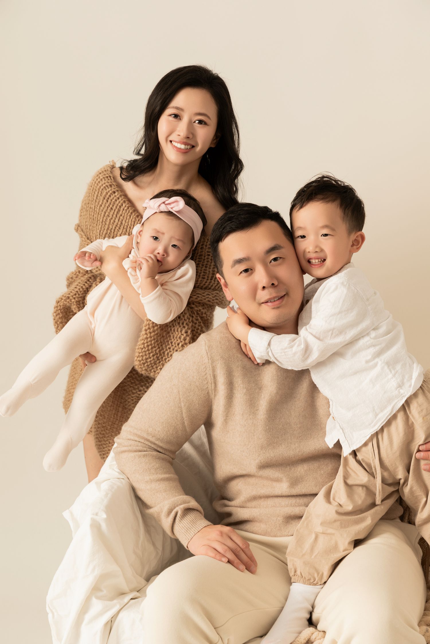 Studio portrait with neutral tones showing playful family moment against beige background.