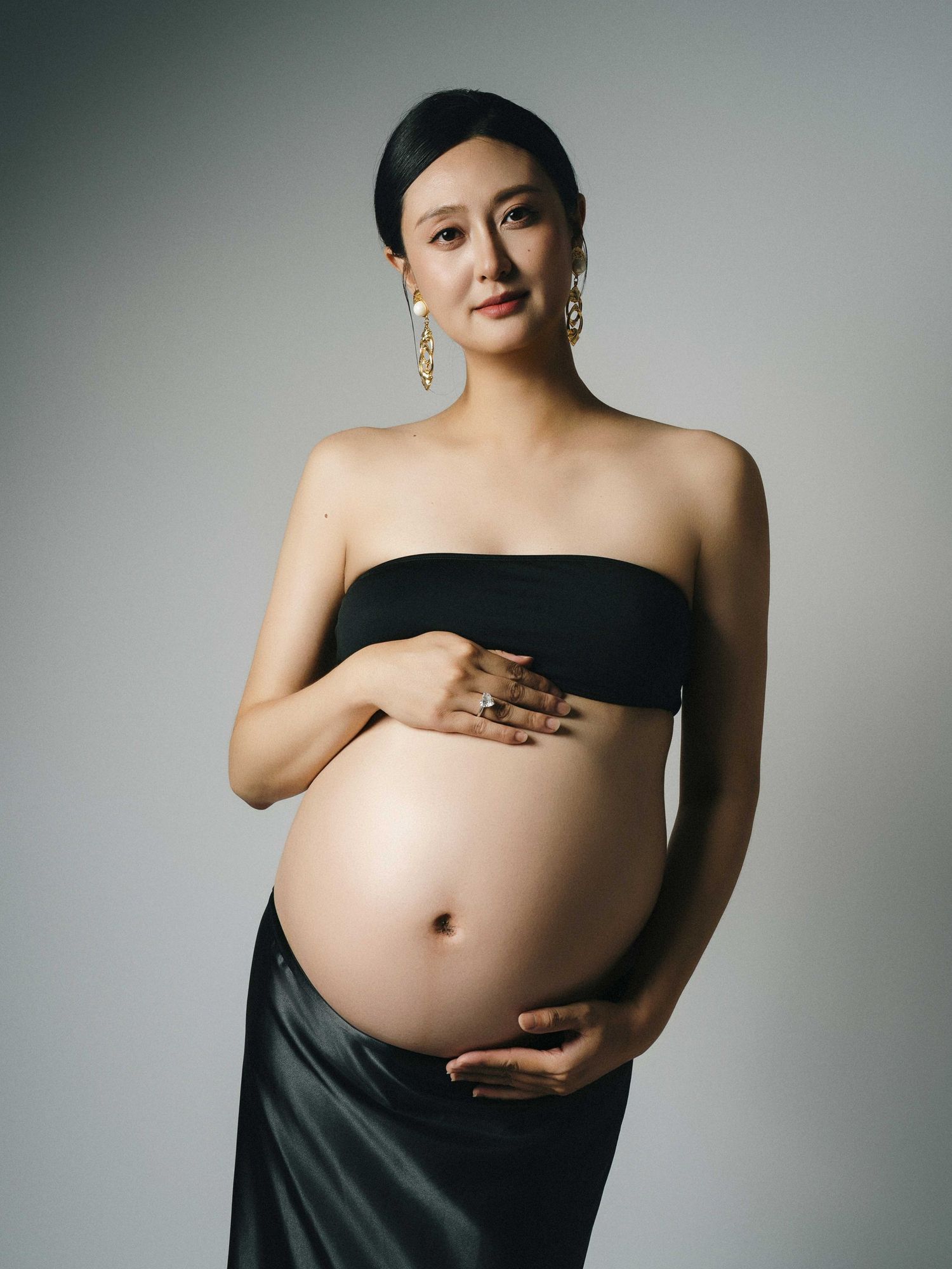 Minimalist maternity photo session with black fabric against grey backdrop.