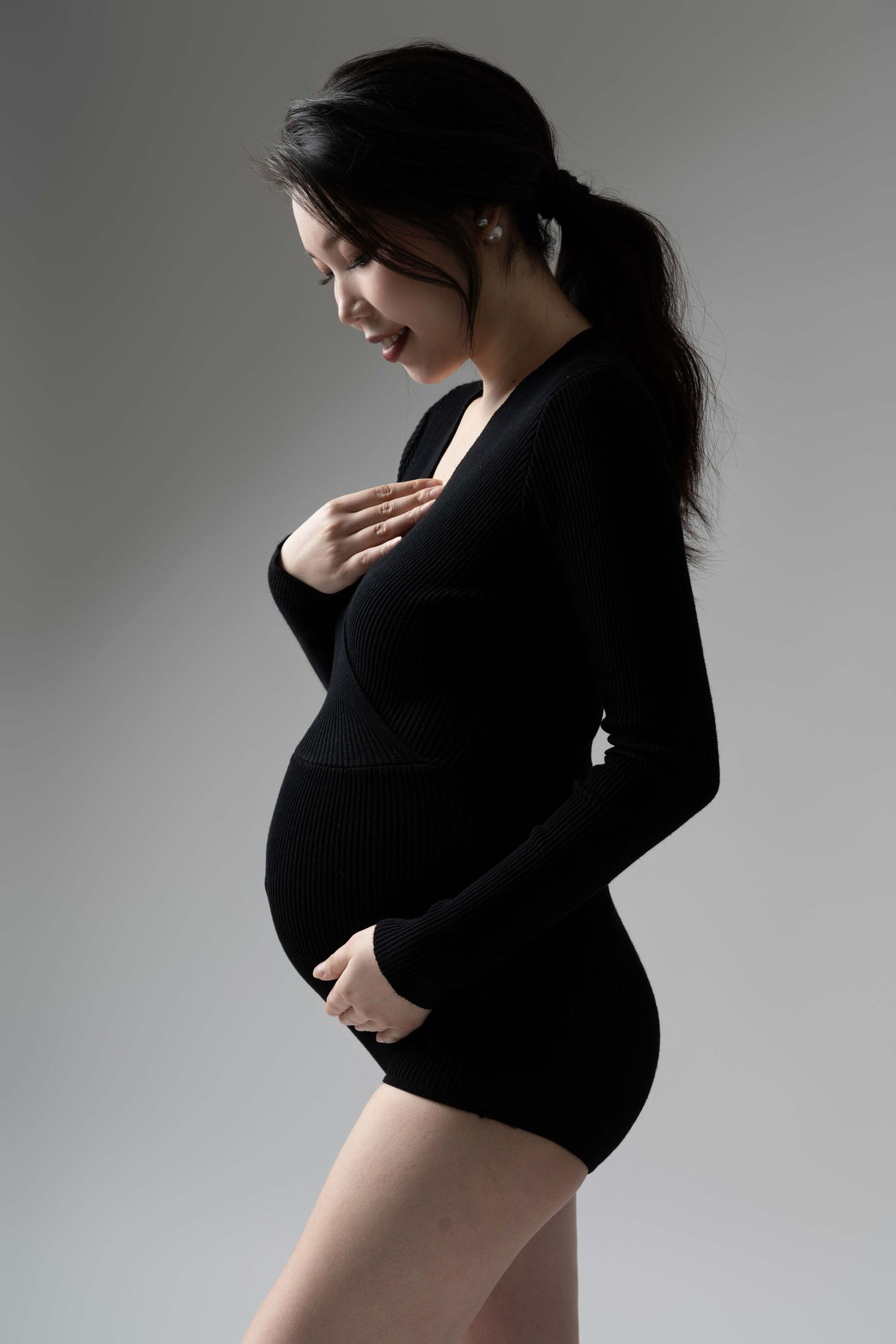 Side profile maternity photos showing pregnancy silhouette in black against grey background.
