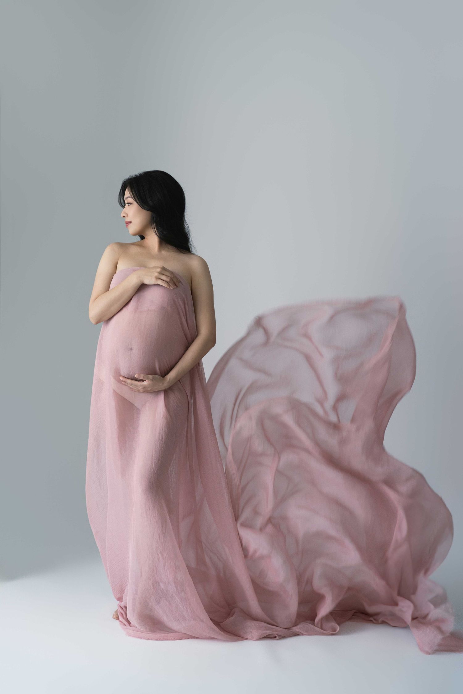 Artistic maternity photos with billowing dusty rose fabric in minimalist setting.