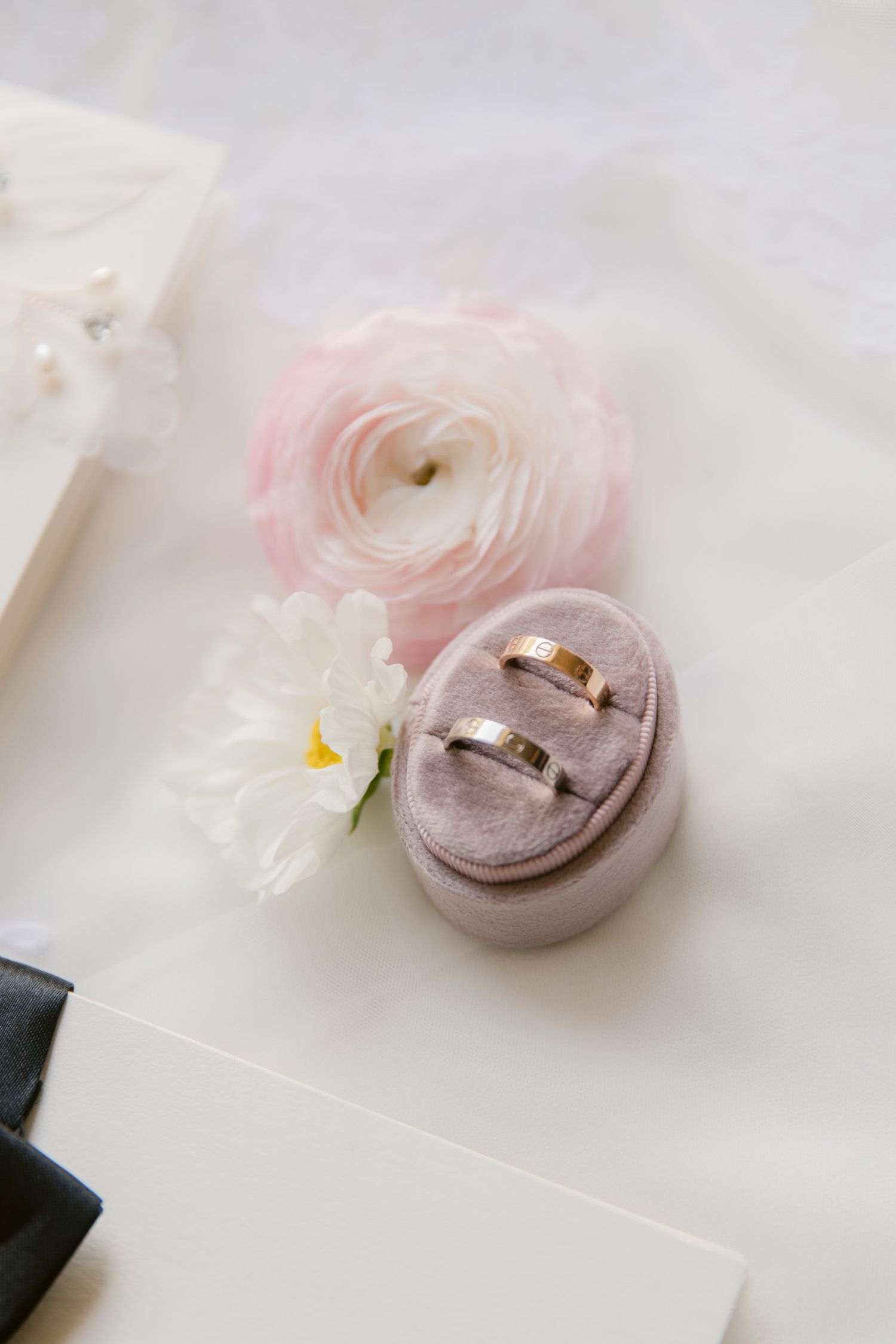 Delicate pink and mauve wedding rings displayed on white fabric with floral accents.