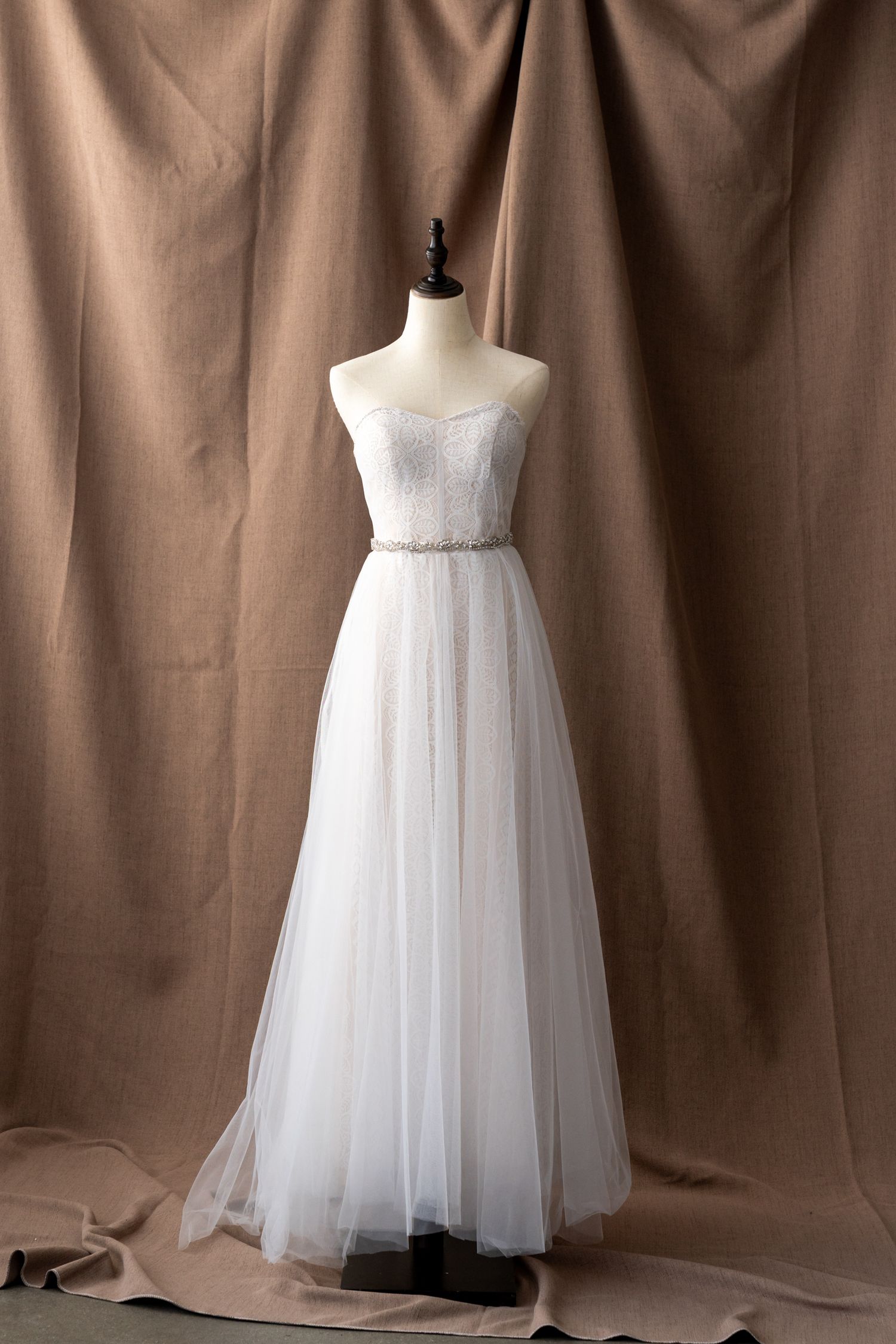 Full-length tulle wedding dress with lace bodice and crystal belt displayed on mannequin.