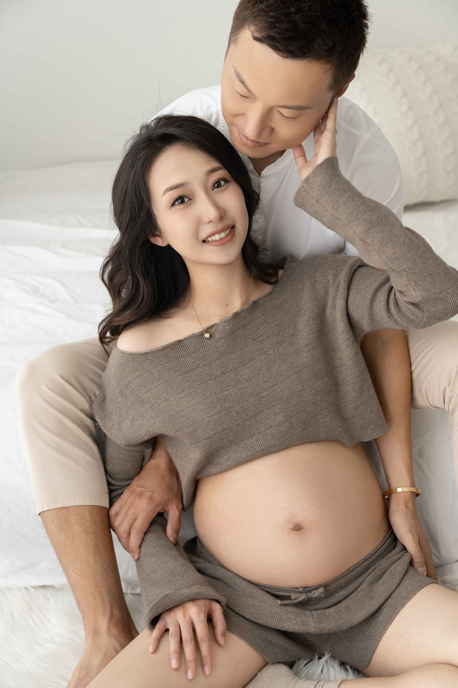 Casual maternity photos of couple relaxing on light colored furniture.