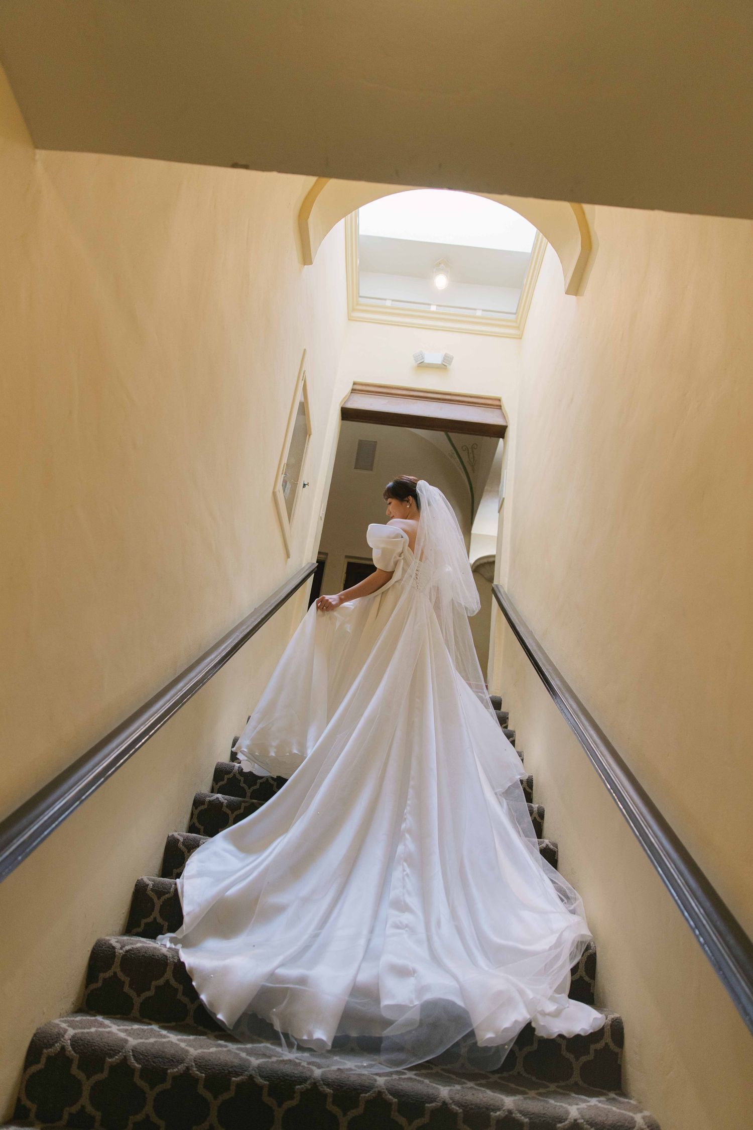 A flowing white wedding dress trails down a staircase hallway.