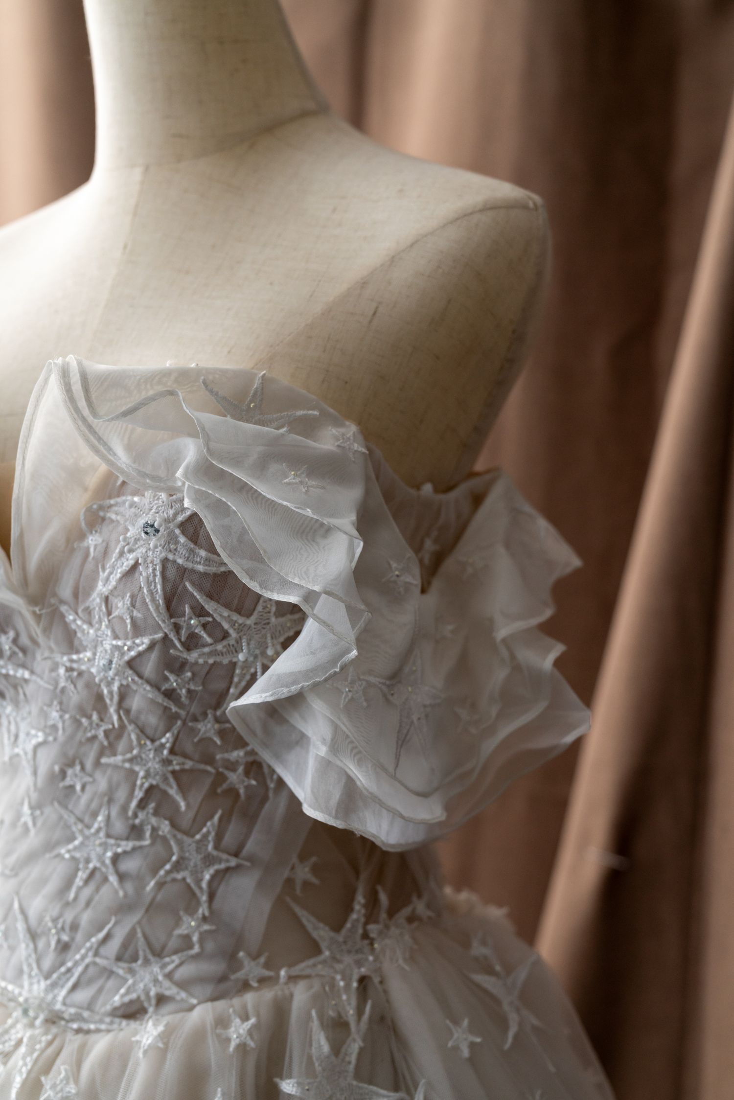 Close-up of wedding dress bodice featuring intricate star-patterned lace and ruffle details.