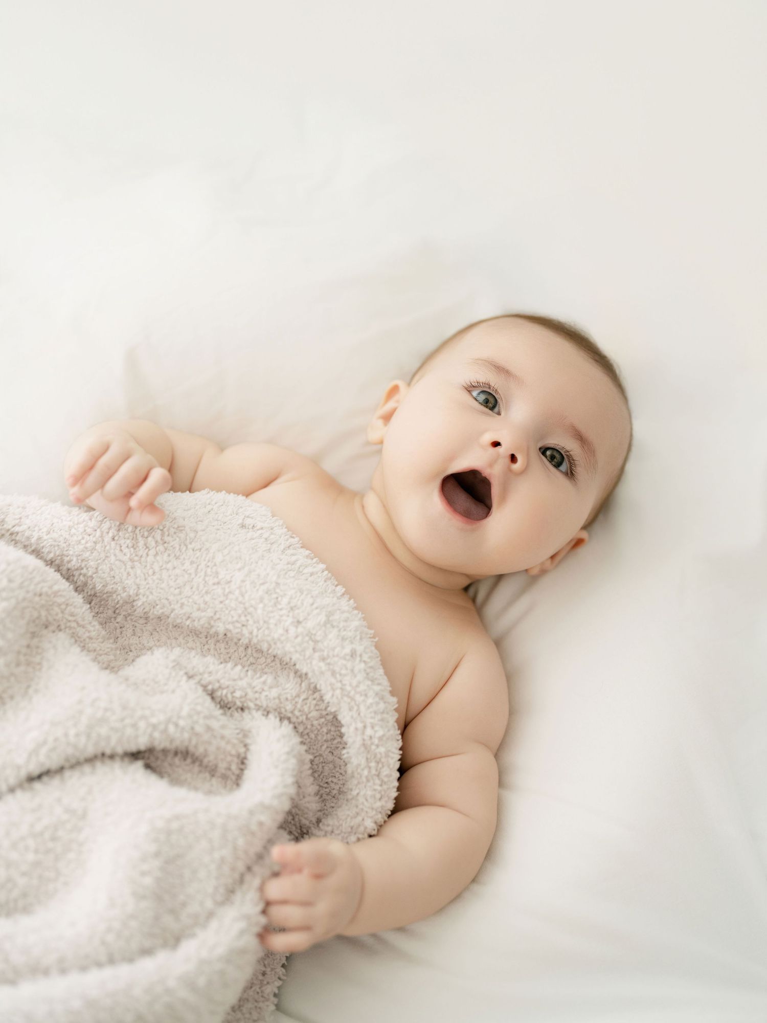 Baby wrapped in cozy grey blanket on white bedding.