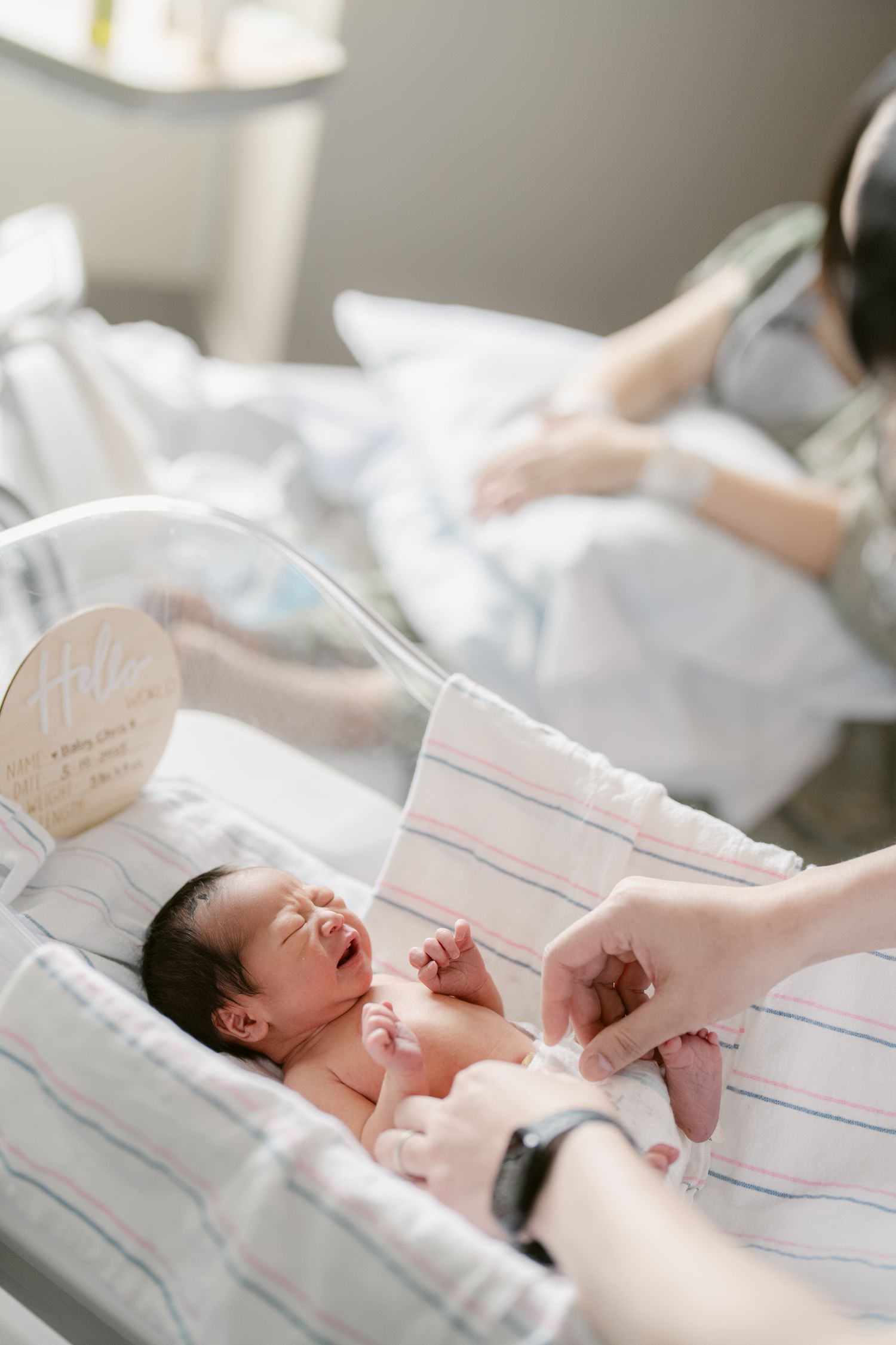 A crying newborn baby receives medical attention in a hospital bassinet.