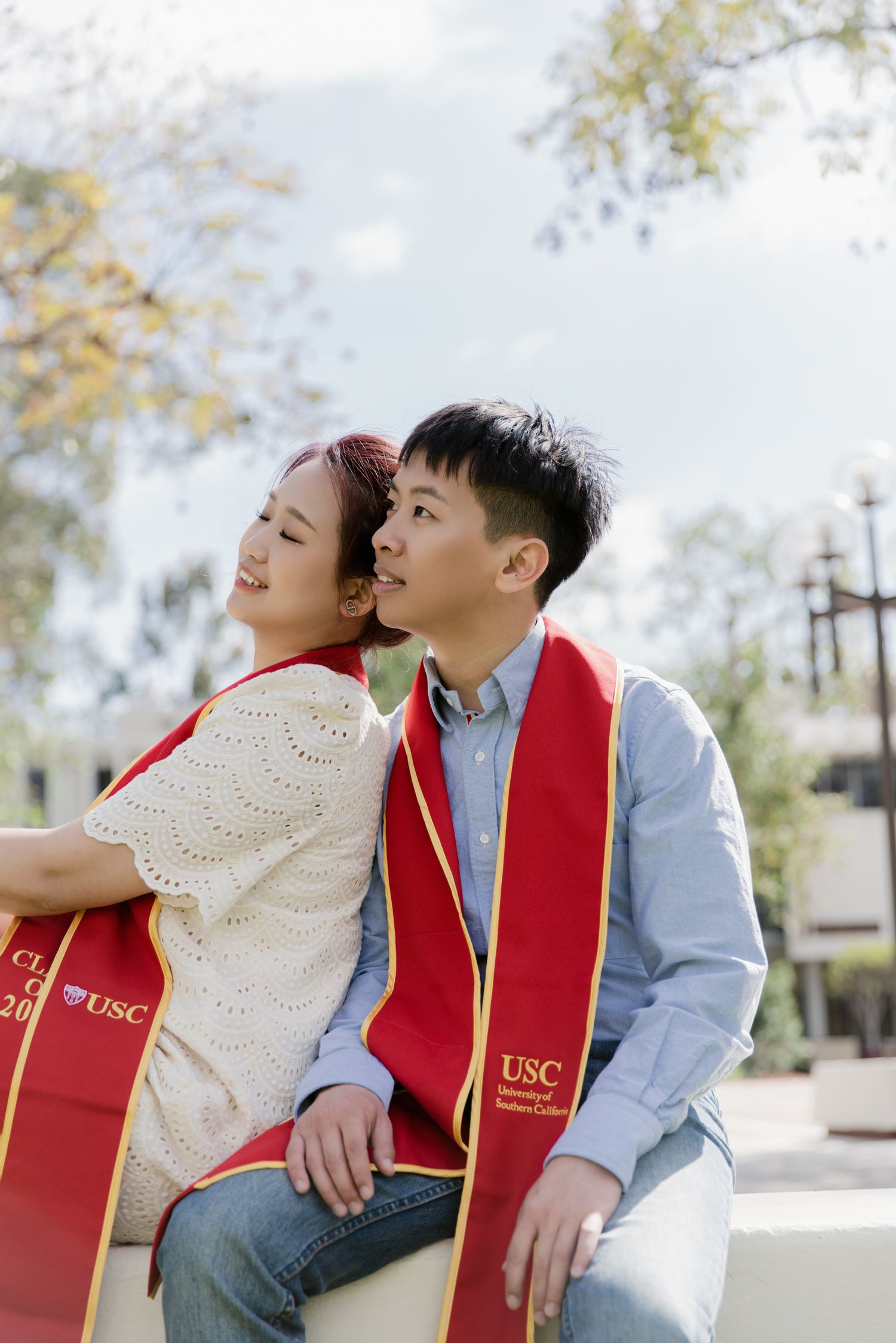 Graduate wearing USC stole and white dress sitting outdoors on campus.