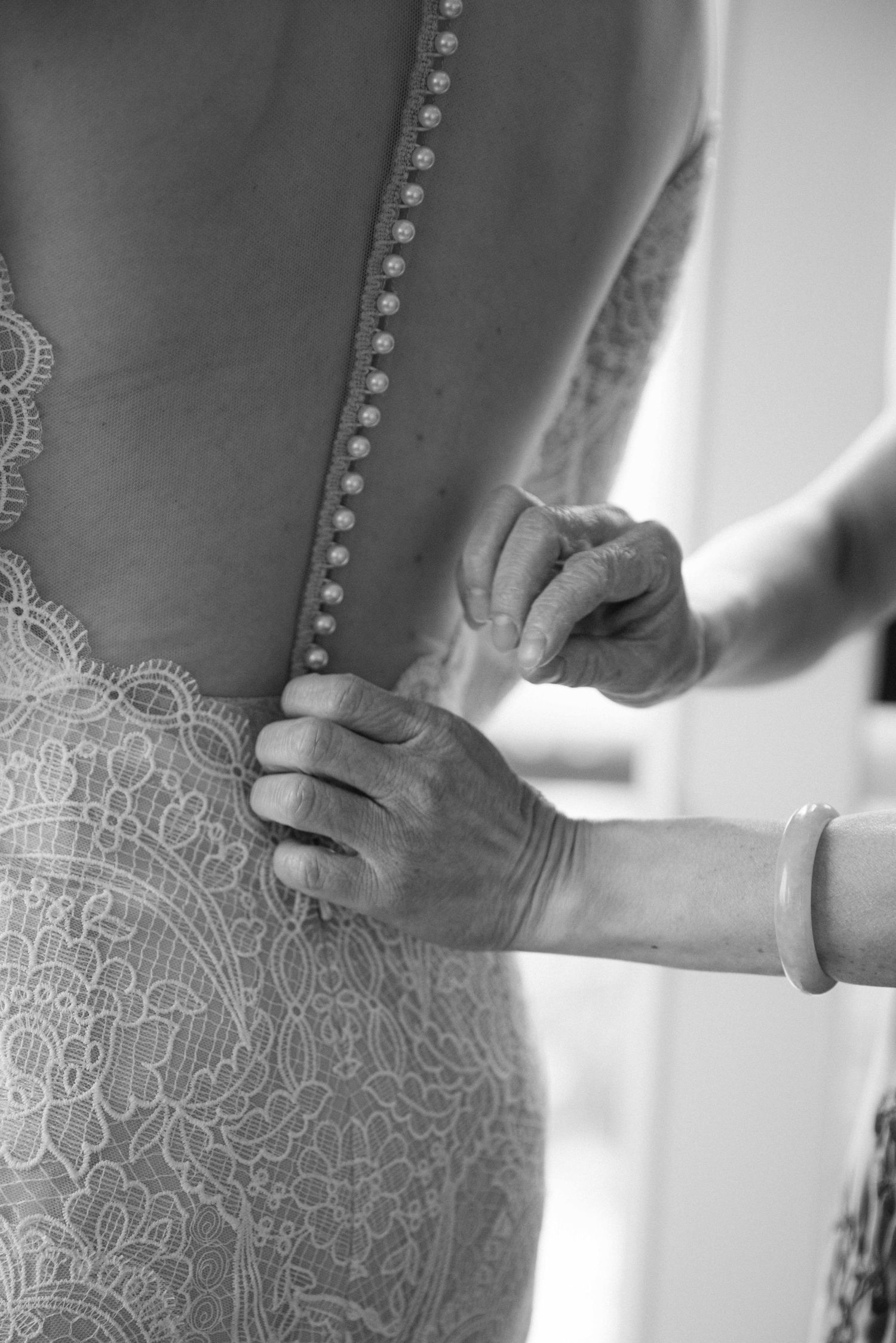 Close-up detail of intricate lace pattern on wedding dress being adjusted.