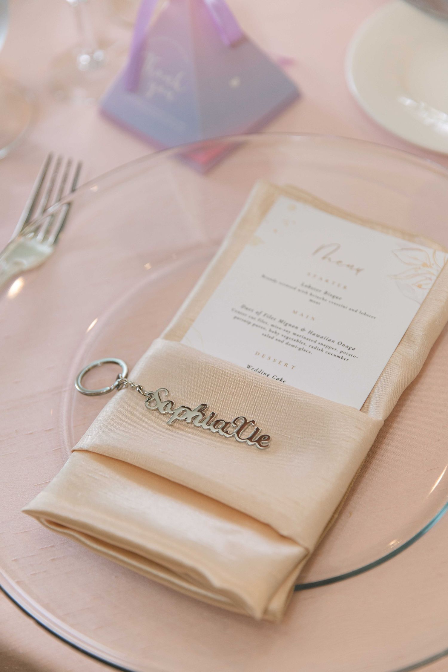 Wedding reception place setting with cream napkin and menu card on pink tablecloth.