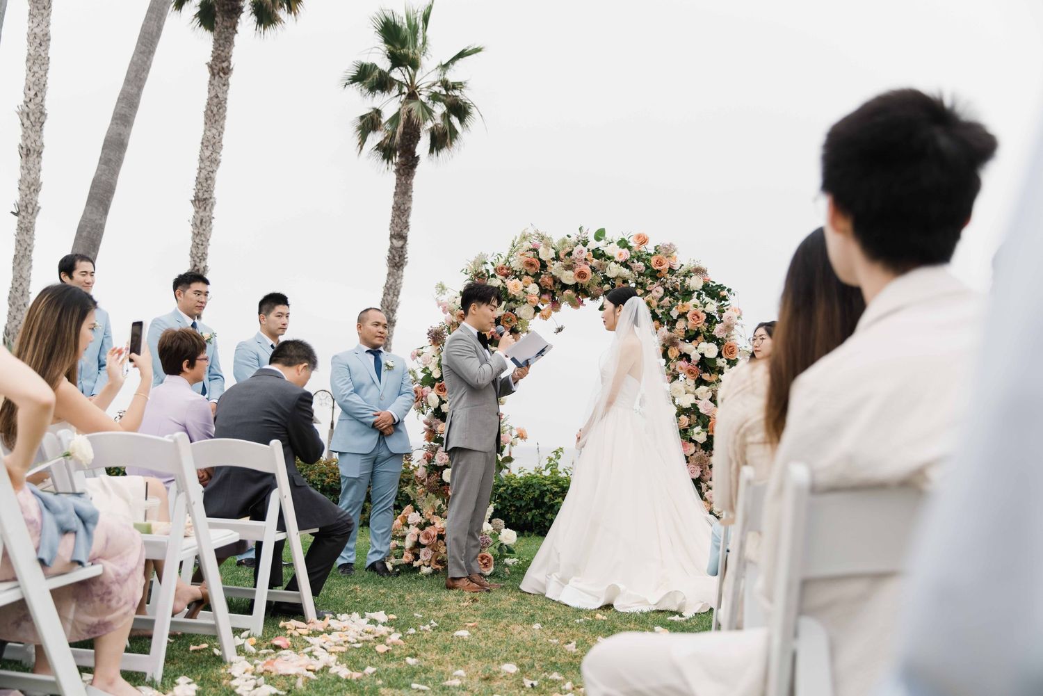 Outdoor wedding ceremony setup with floral arch and palm trees in background.