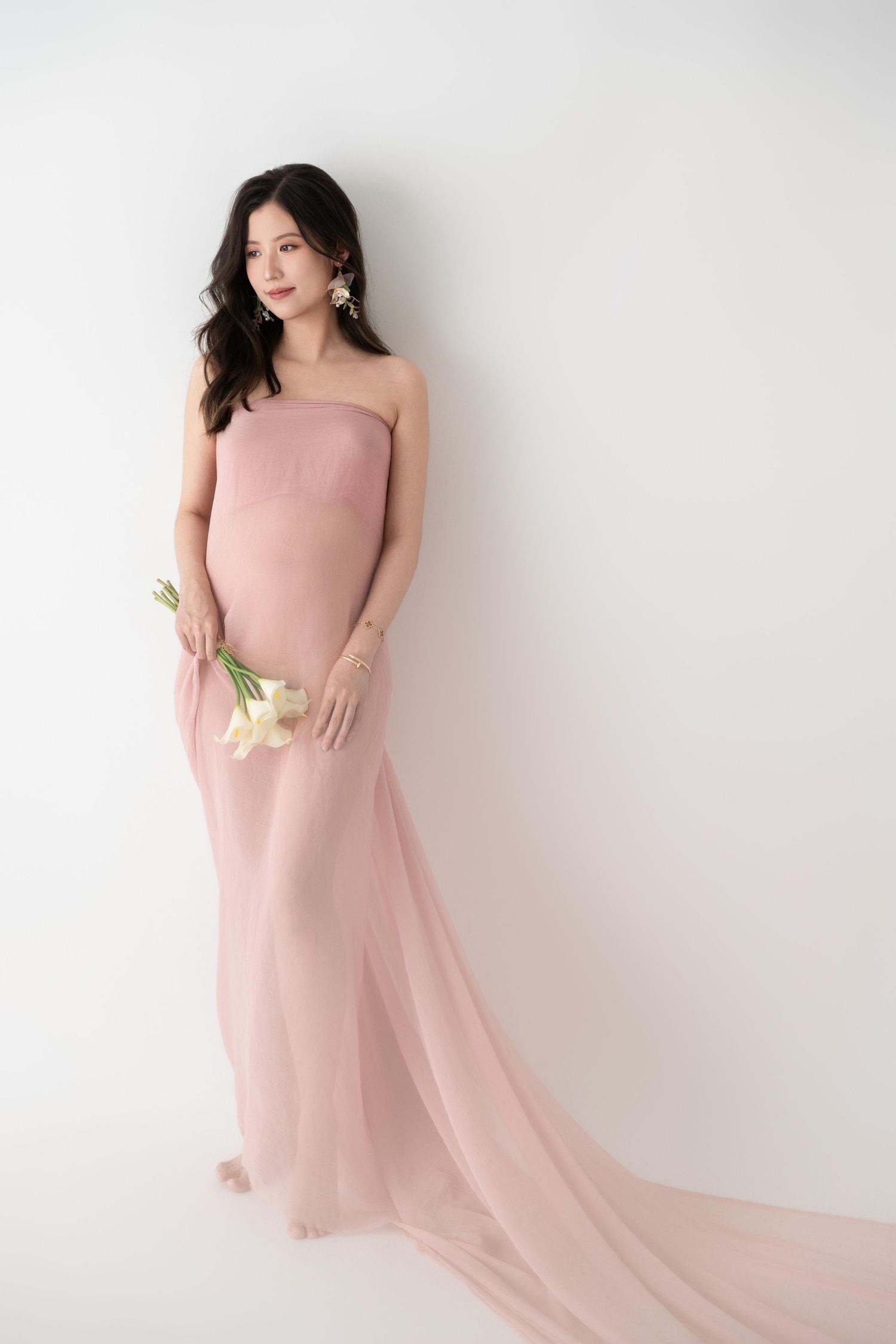 Maternity photoshoot featuring flowing pink dress against white backdrop.