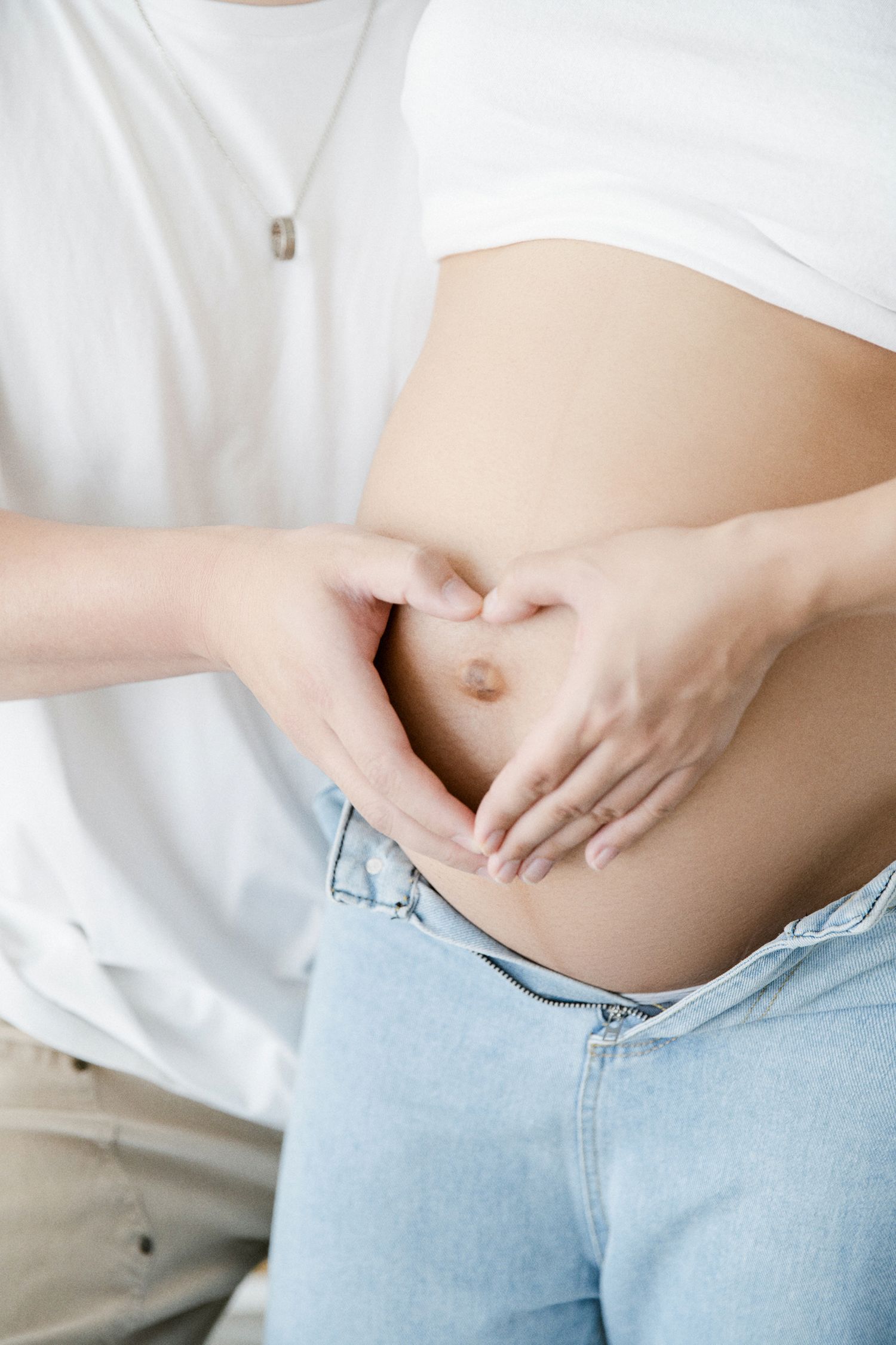 Hands forming heart shape on pregnant belly wearing denim jeans.