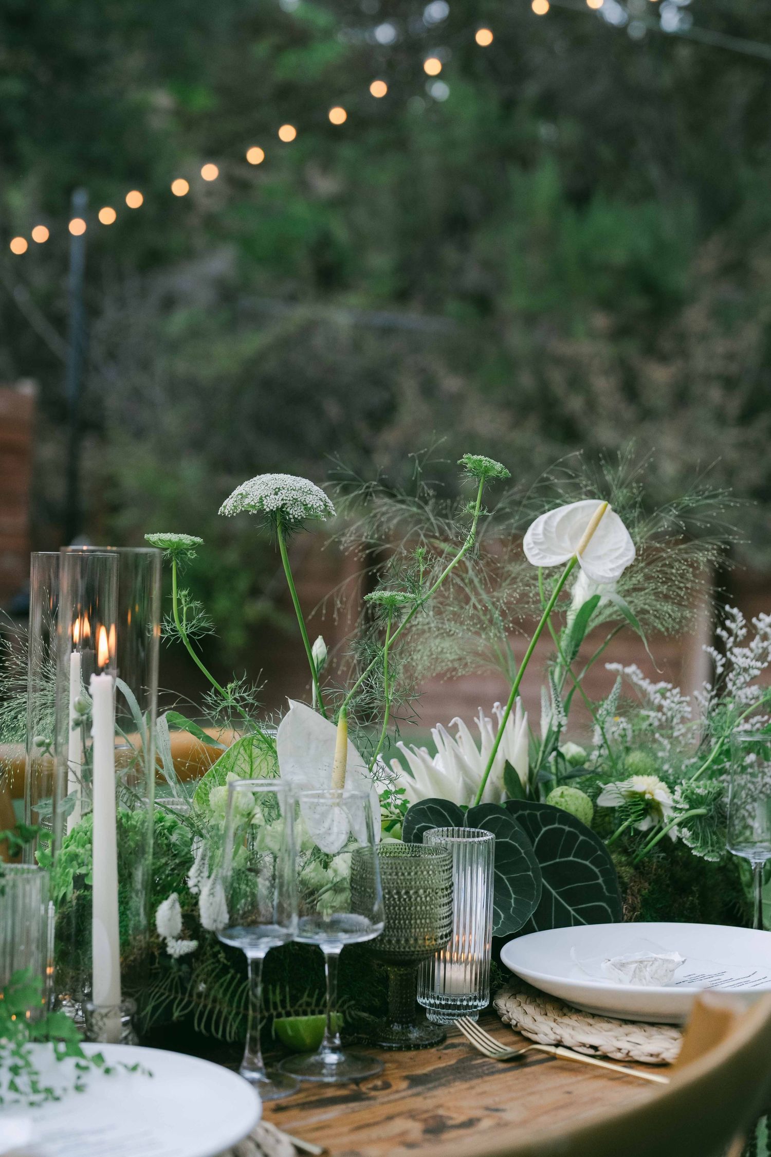 Garden-style table decor with white candles, glass vessels, and fresh greenery.
