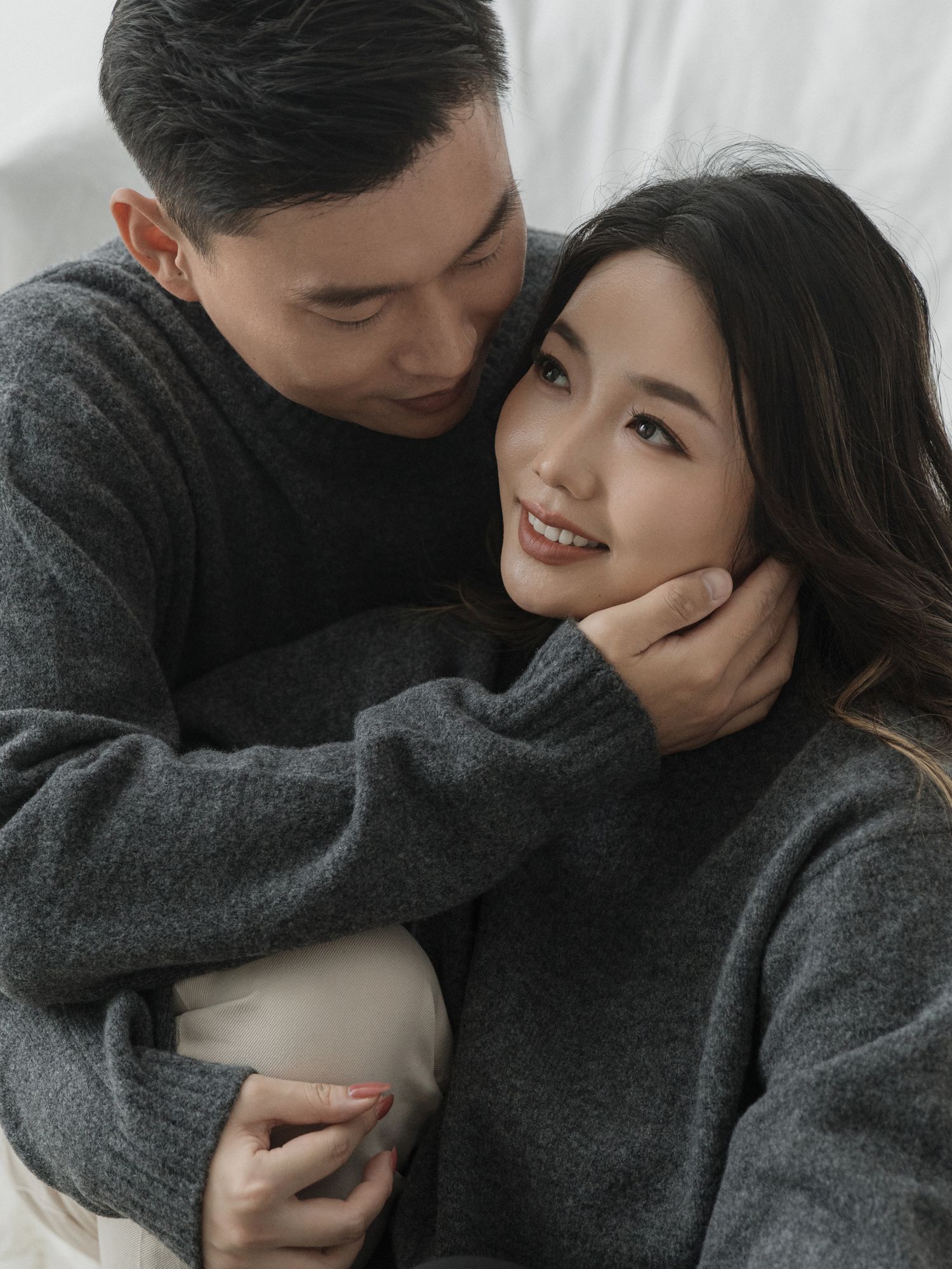 Romantic couple embracing and sharing playful moments while wearing matching gray sweaters.