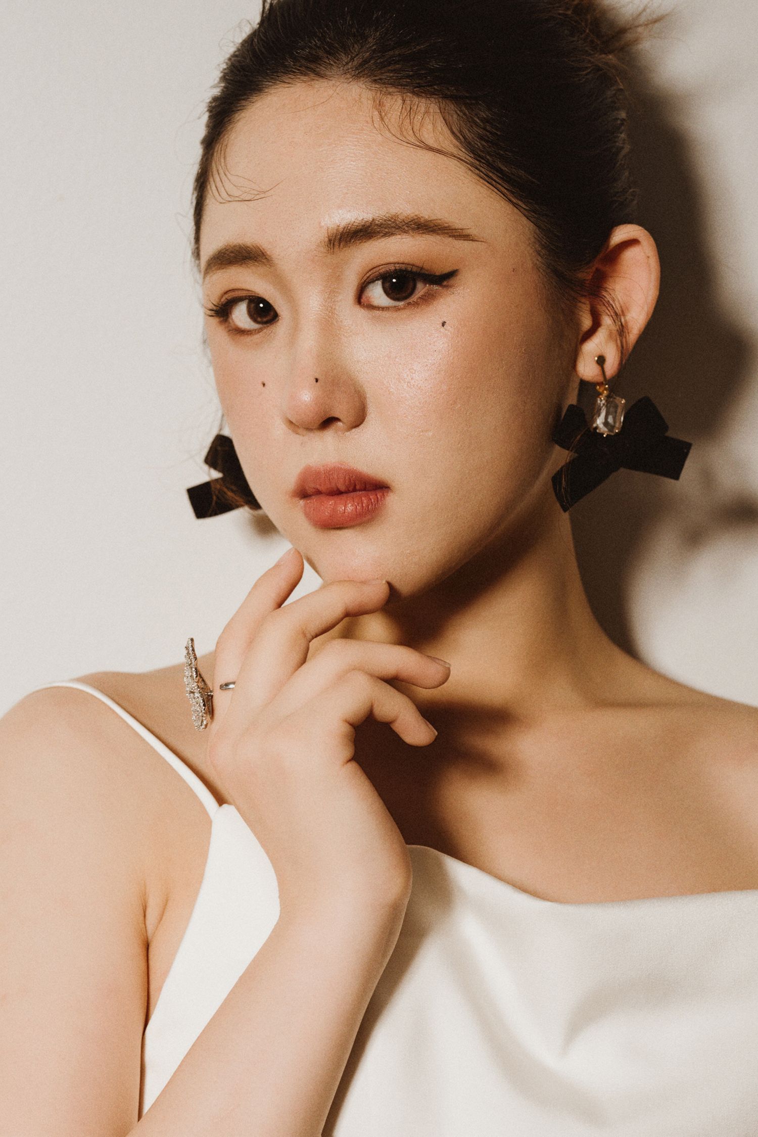 Close-up portrait showing delicate makeup and black hair accessories against beige background.