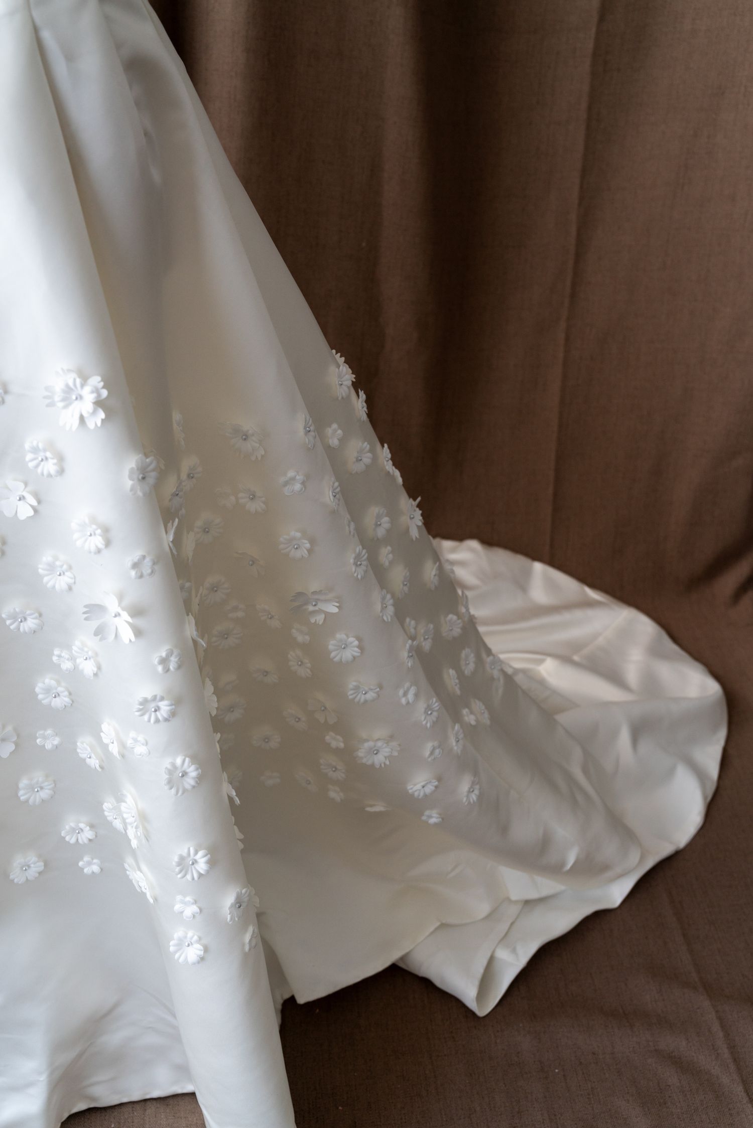 Close-up detail of white floral appliques on a wedding dress skirt against a brown backdrop.