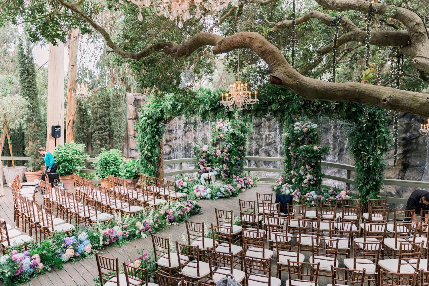 Outdoor wedding ceremony setup with wooden chairs and floral decorations in a lush garden setting.