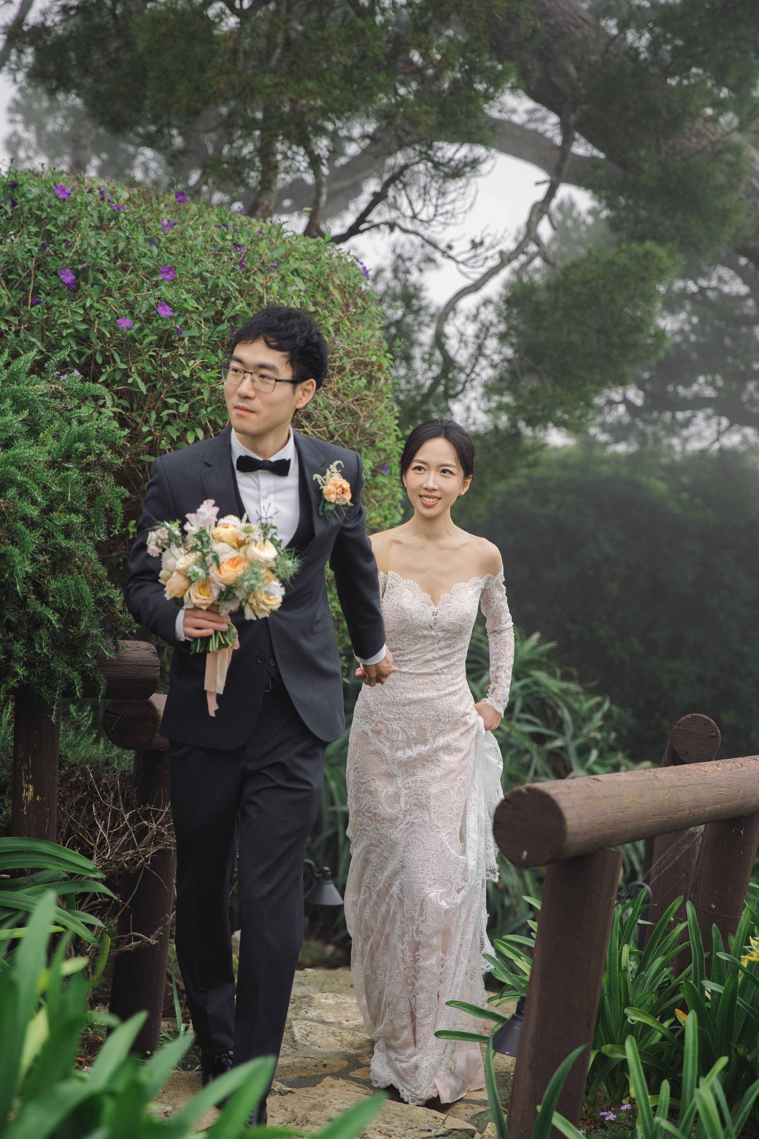 Wedding couple walking along a garden path surrounded by lush greenery.